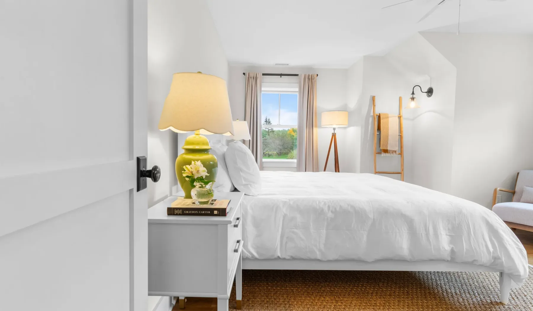 Un dormitorio luminoso con una cama blanca y una ventana con vistas a la vegetación.