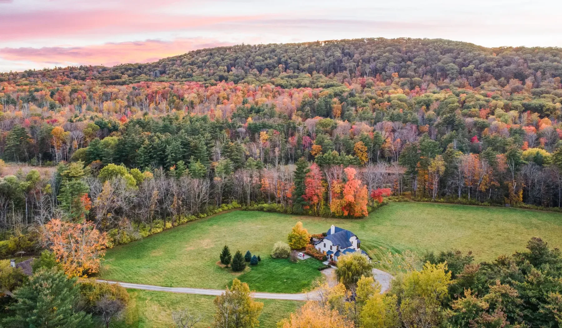 Vista aérea de una casa junto a un campo abierto, rodeada de árboles otoñales de colores.
