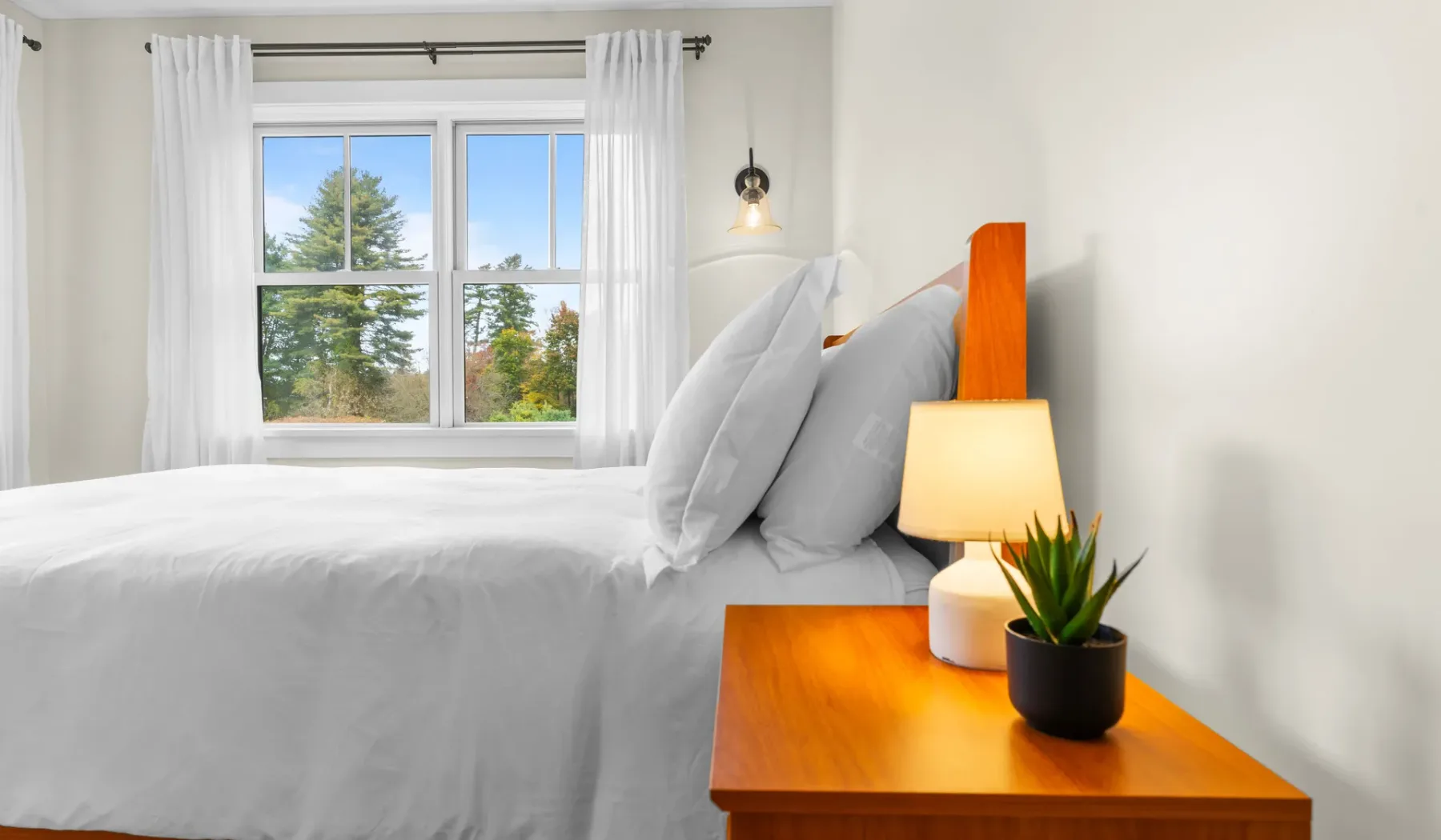 Un dormitorio luminoso con una cama bien tendida junto a una ventana.