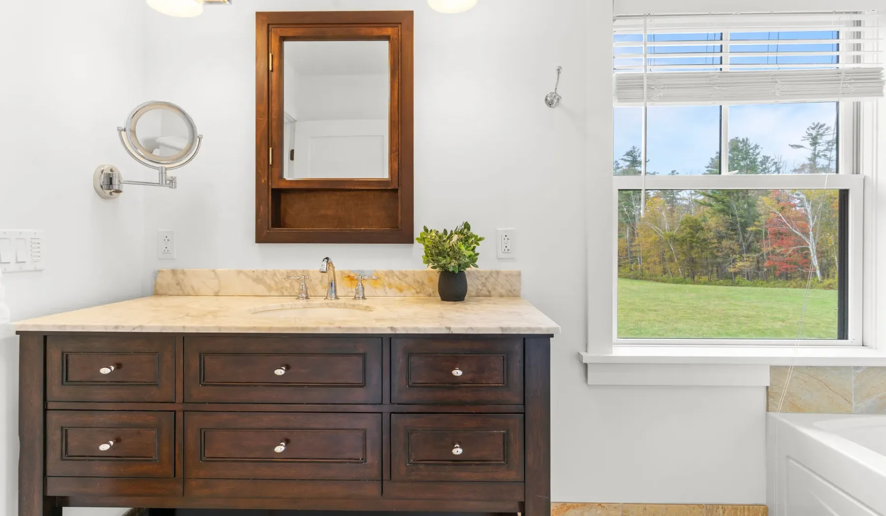 Un tocador de baño con espejo y una ventana con vista a un césped.