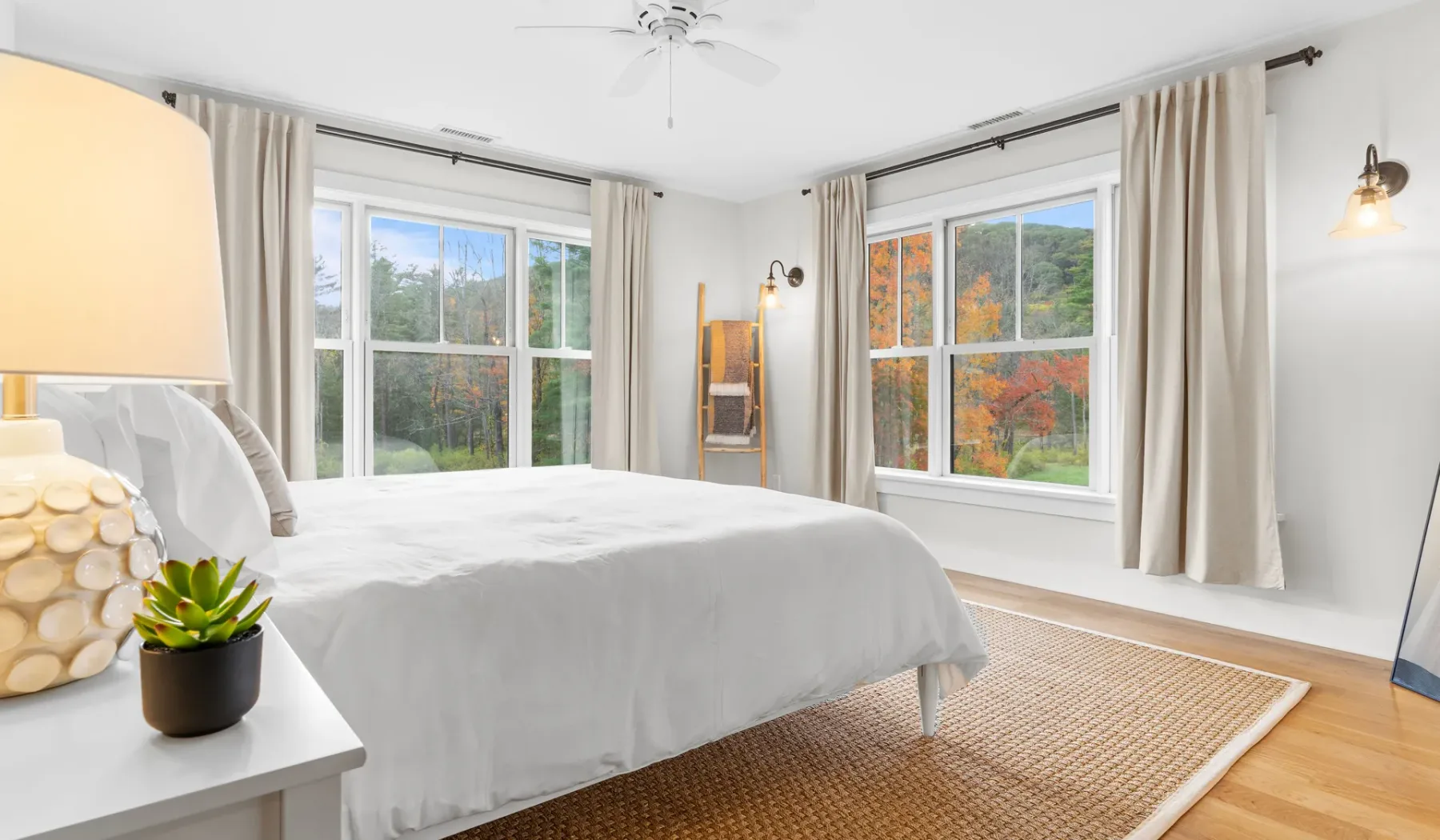 Un dormitorio luminoso con una cama junto a grandes ventanas y cortinas claras.