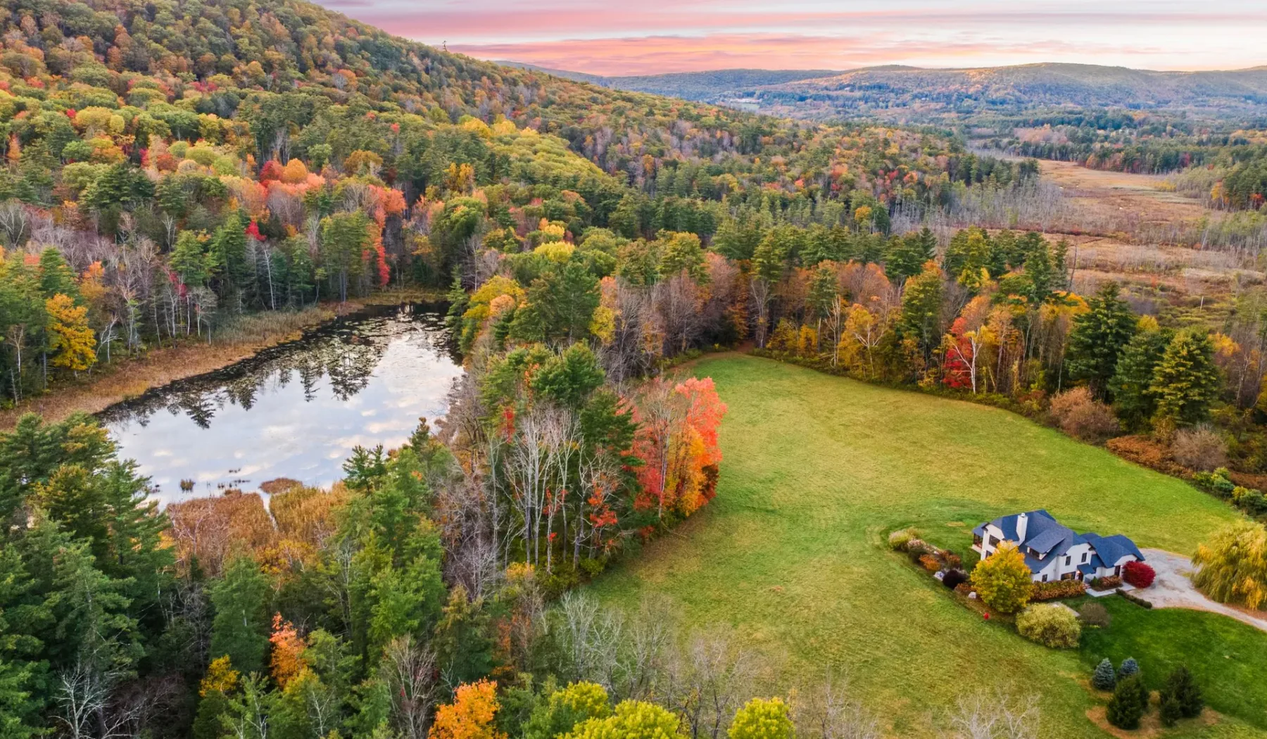 Vista aérea de una casa rural junto a un estanque y árboles otoñales de colores.