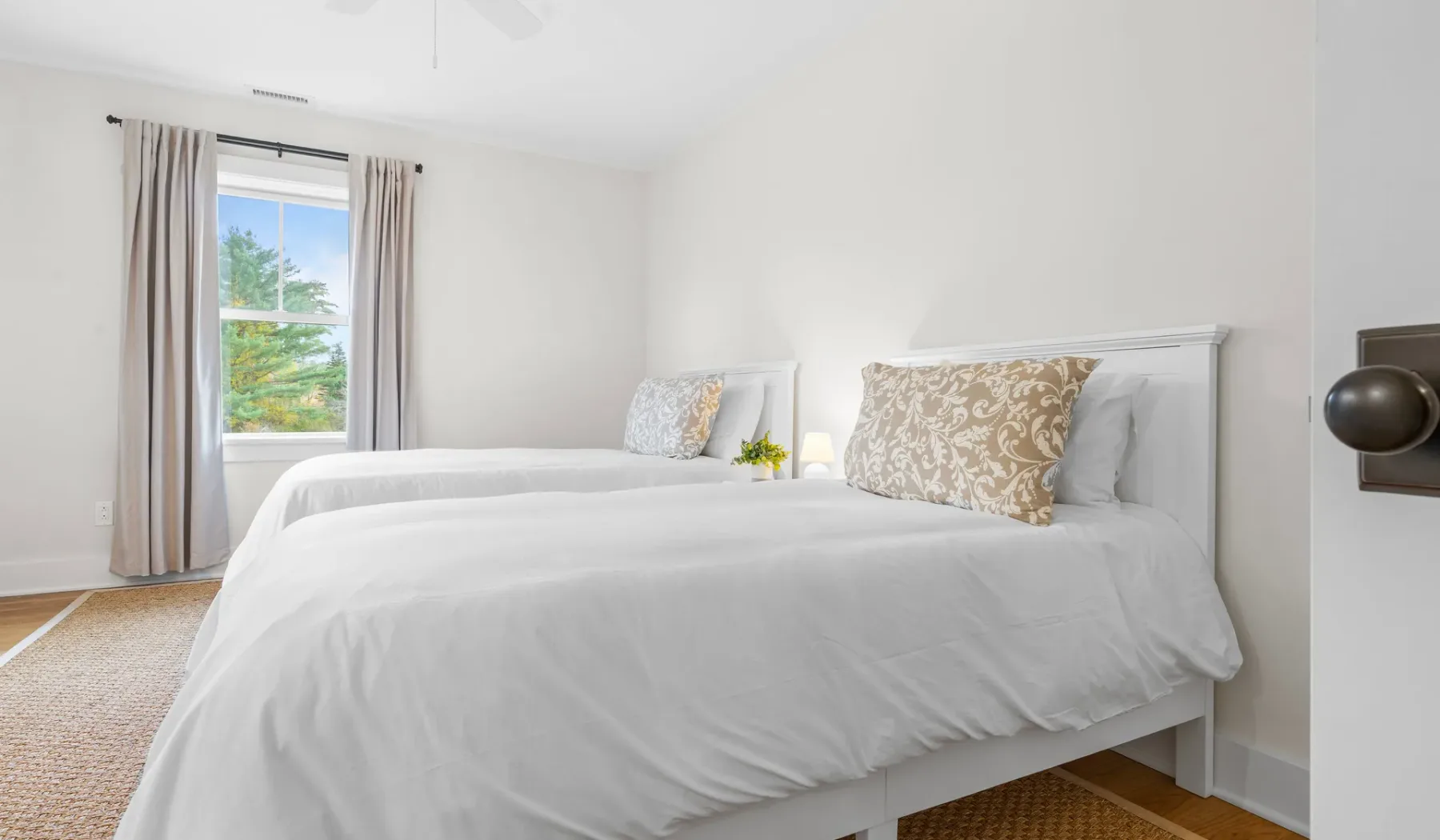 Un dormitorio luminoso con ropa de cama blanca y una ventana con cortinas.