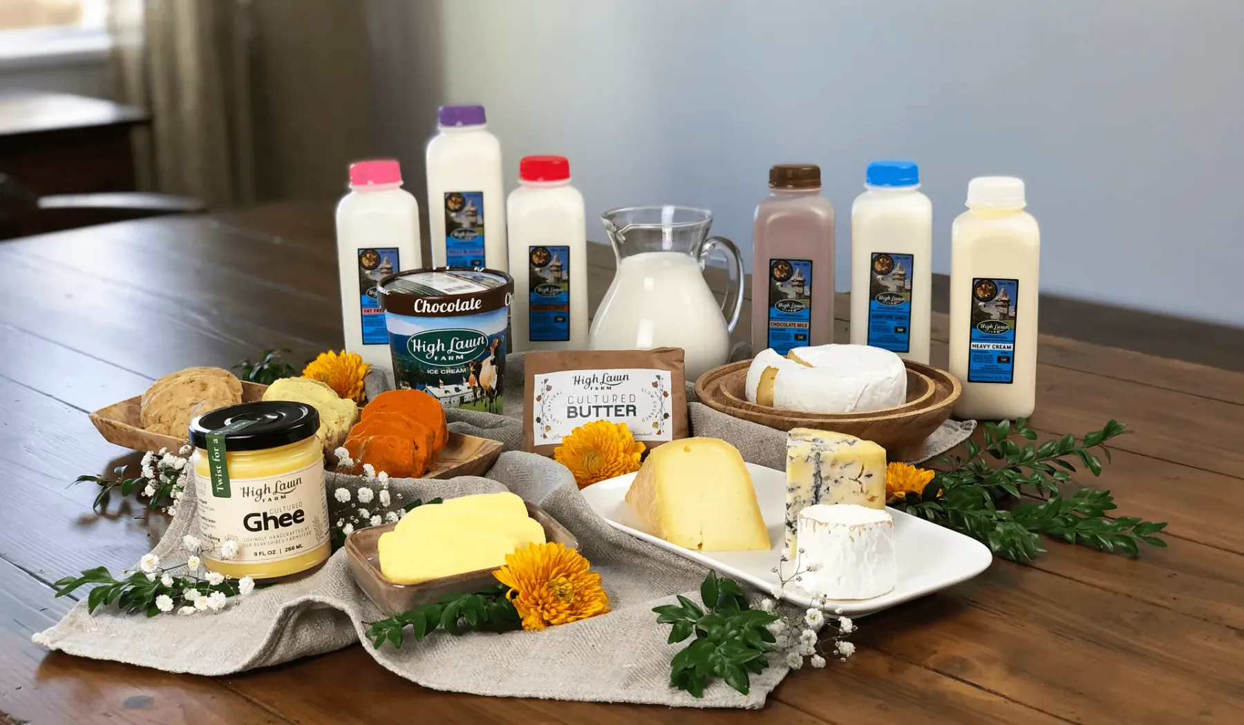 Una presentación sobre una mesa de productos lácteos, con frascos, botellas, mantequilla y queso.