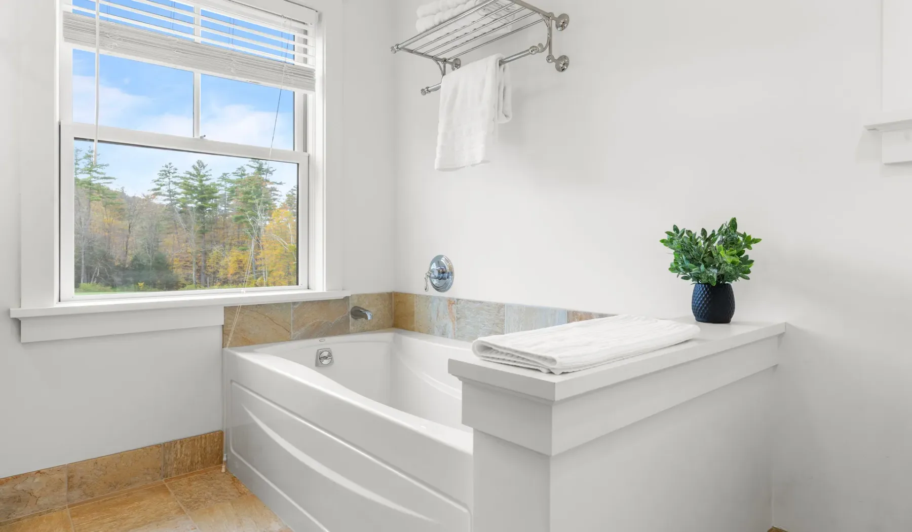 Un baño luminoso con una bañera empotrada bajo una ventana grande.