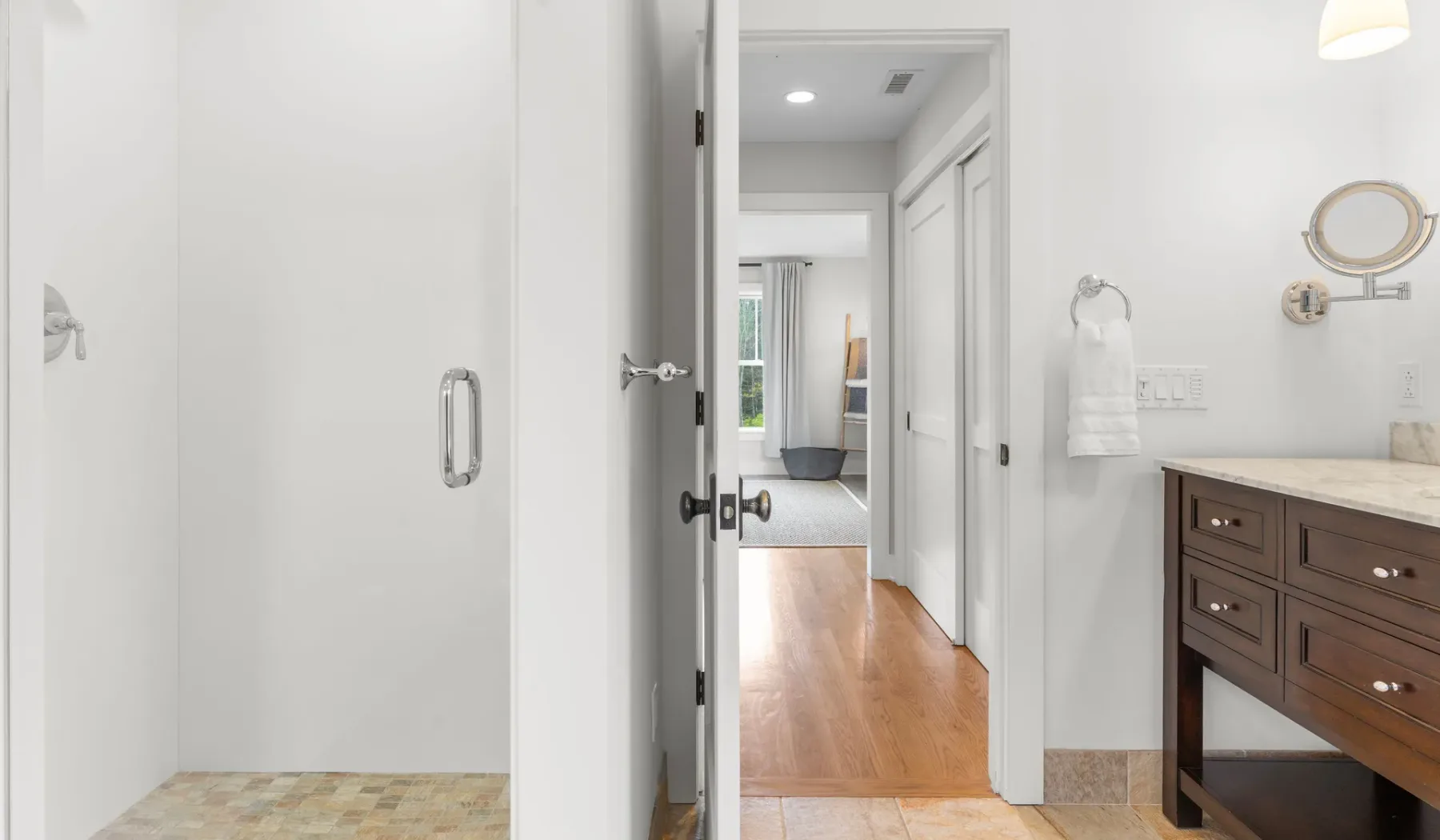 Un baño luminoso con un tocador de madera y una puerta abierta hacia un pasillo.