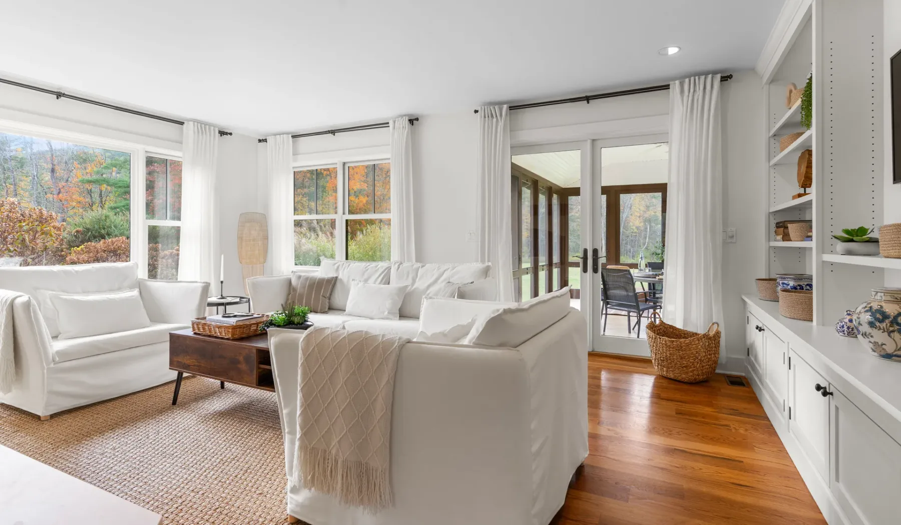 Una sala luminosa con asientos blancos, ventanas amplias y una mesa de centro de madera.