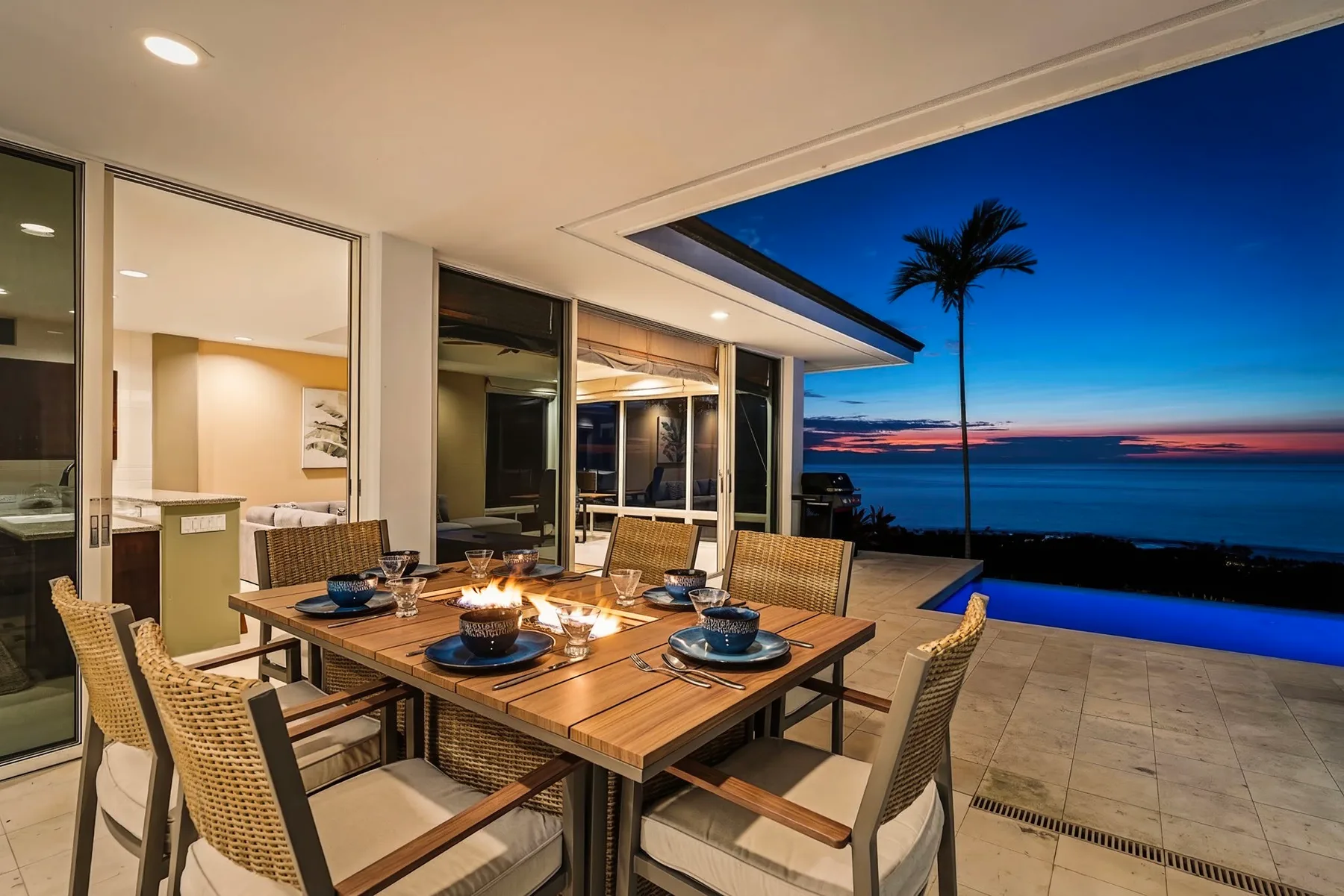 Un comedor al aire libre se abre a una piscina y vistas al mar al atardecer.