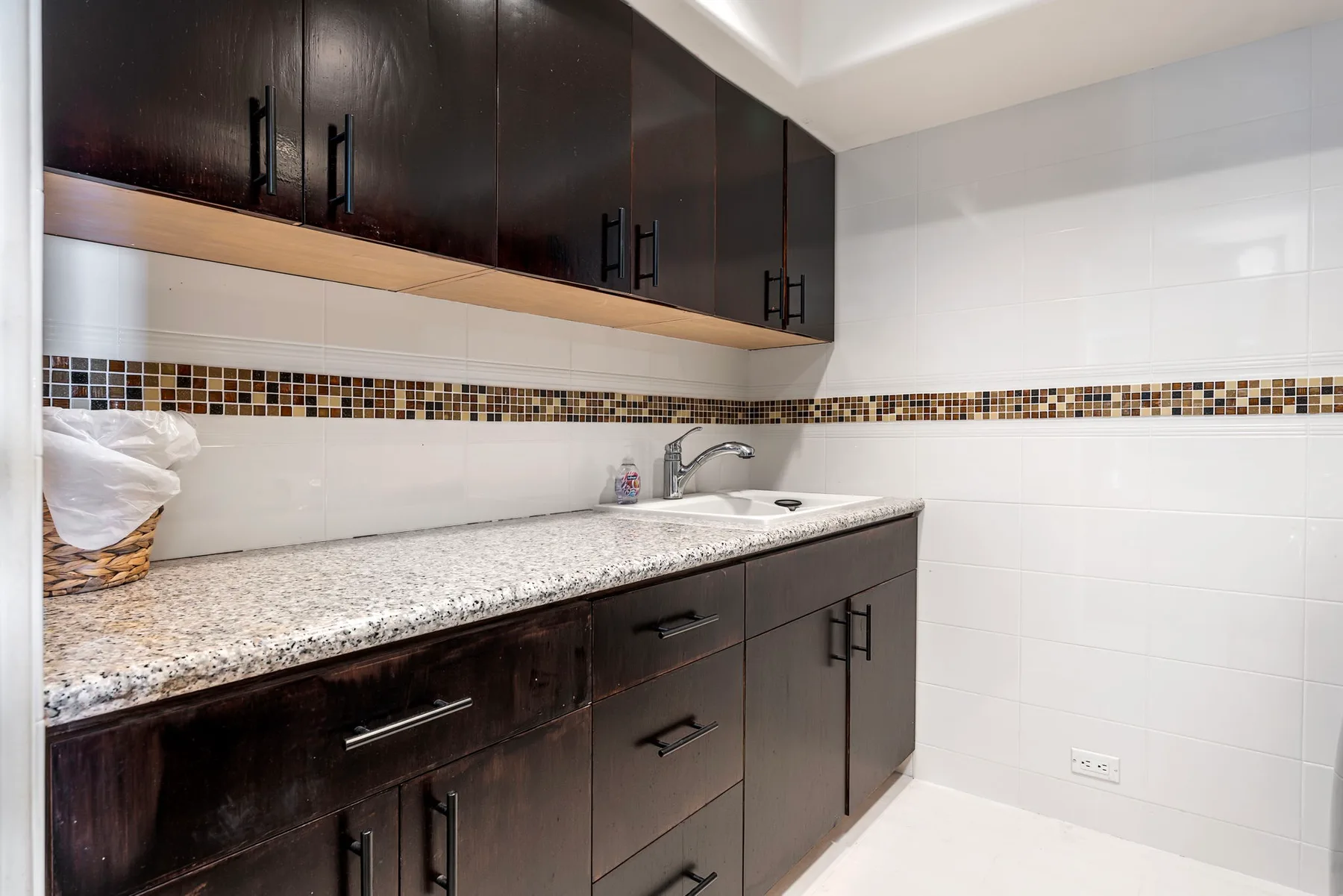 Un tocador de baño con gabinetes oscuros, una encimera moteada y paredes revestidas de azulejos.