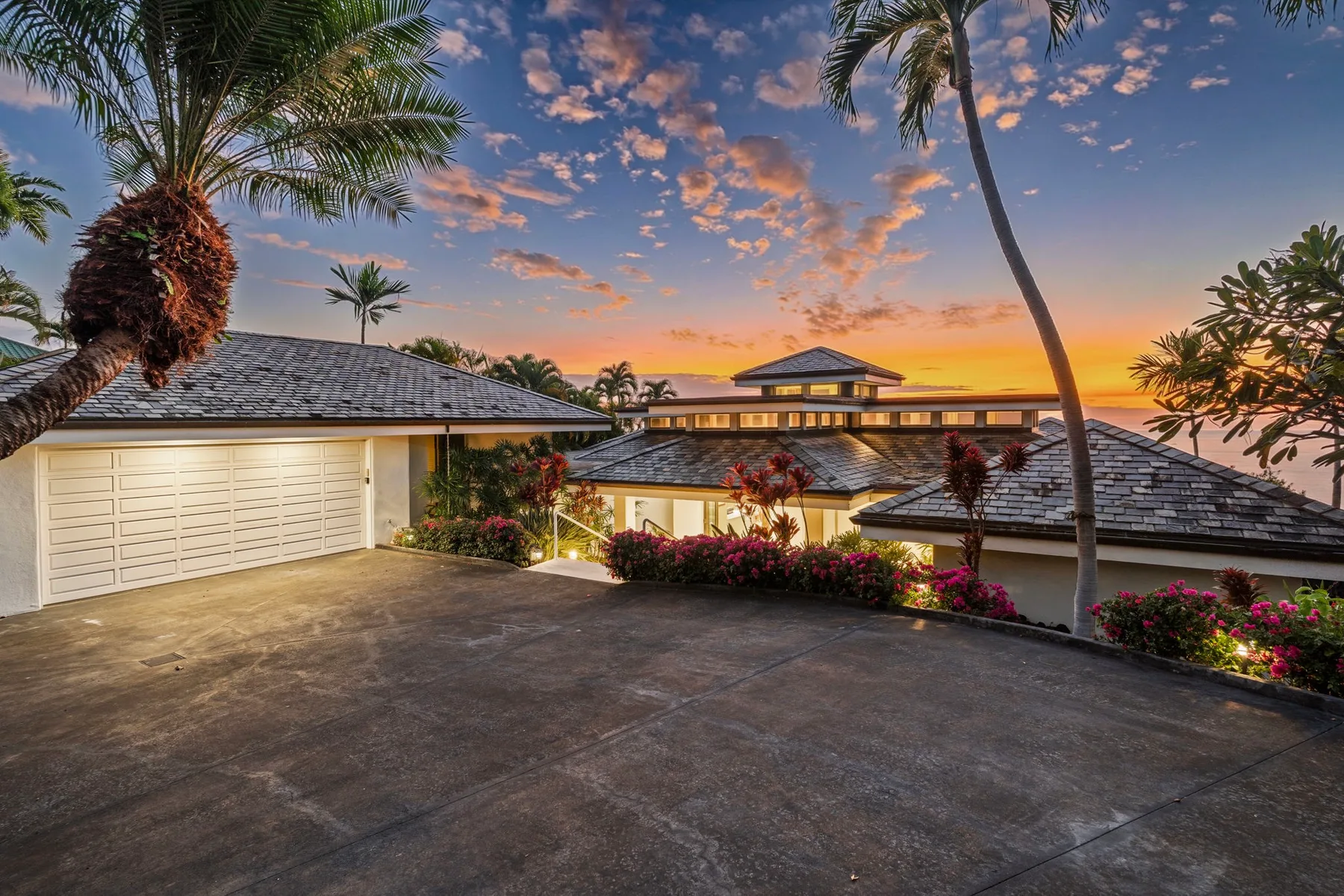 Una casa tropical y una entrada pavimentada dan al océano al atardecer.