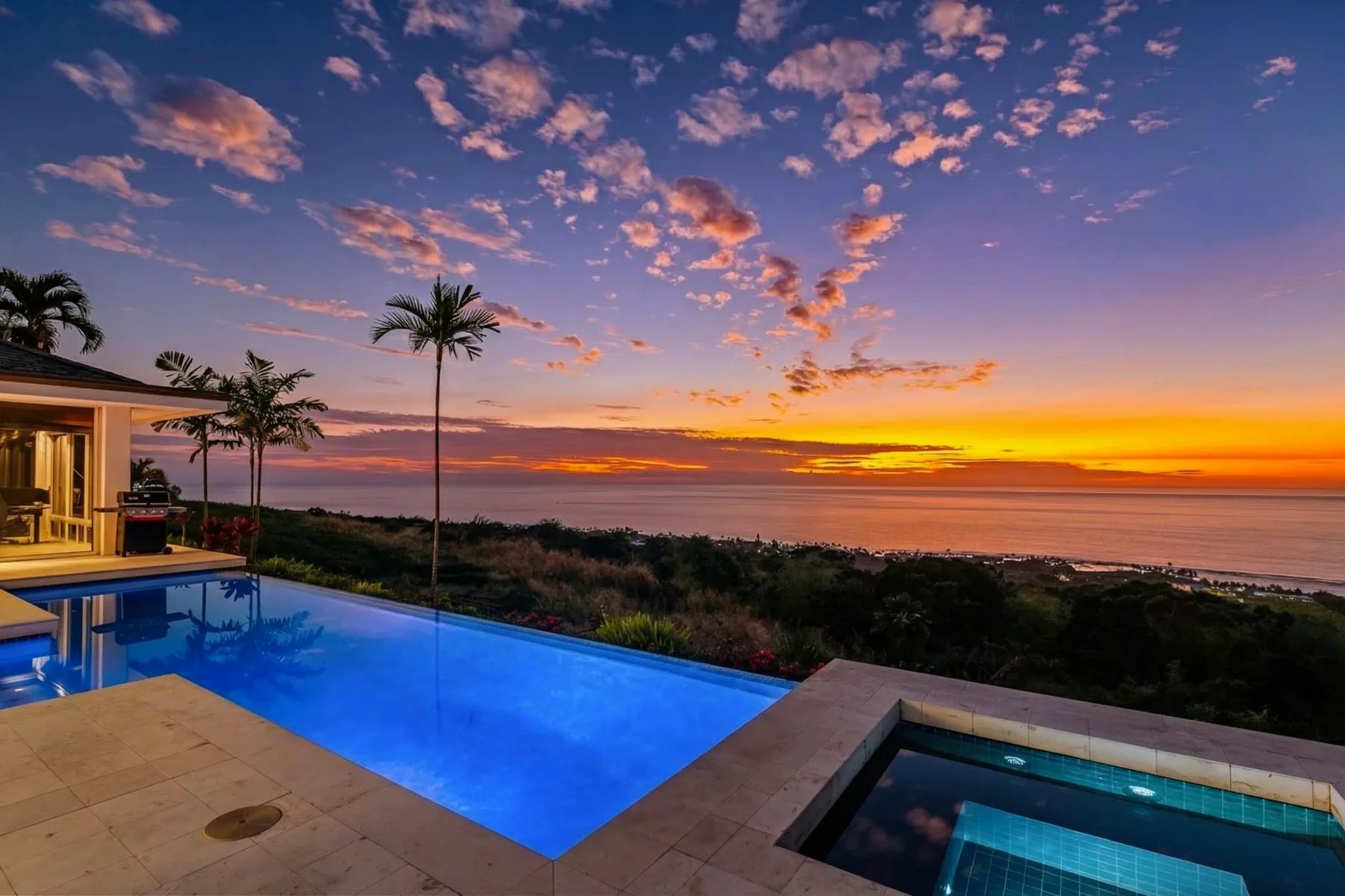 Una piscina al aire libre tiene vistas a la costa bajo un cielo de atardecer colorido.