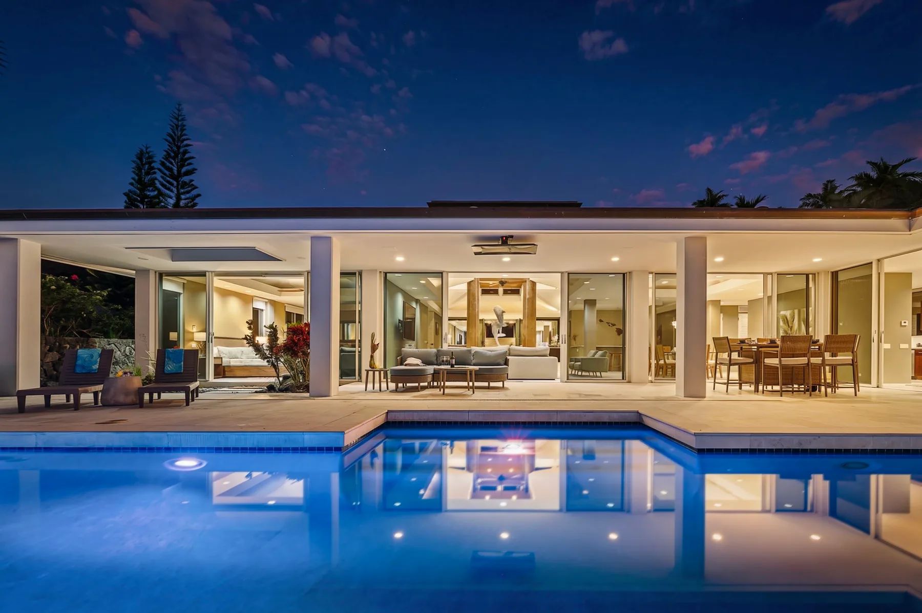Una casa moderna se abre a una piscina, con asientos al aire libre y un comedor.