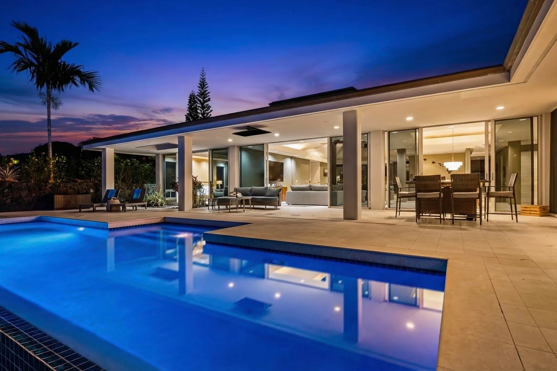 Una casa moderna se abre a una piscina iluminada al anochecer.