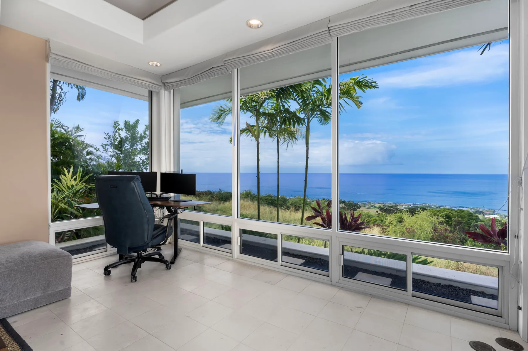 Una luminosa zona de trabajo con escritorio y asientos junto a grandes ventanas con vistas al mar.
