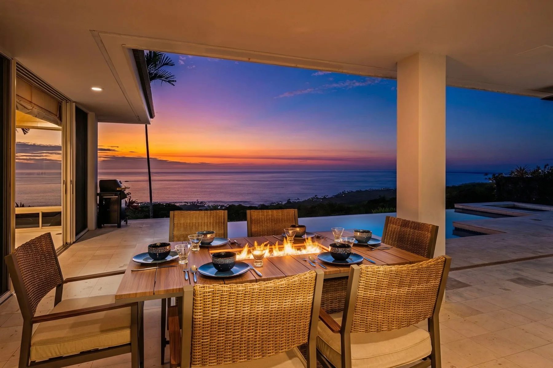 Una zona de comedor al aire libre tiene vistas al océano al atardecer.