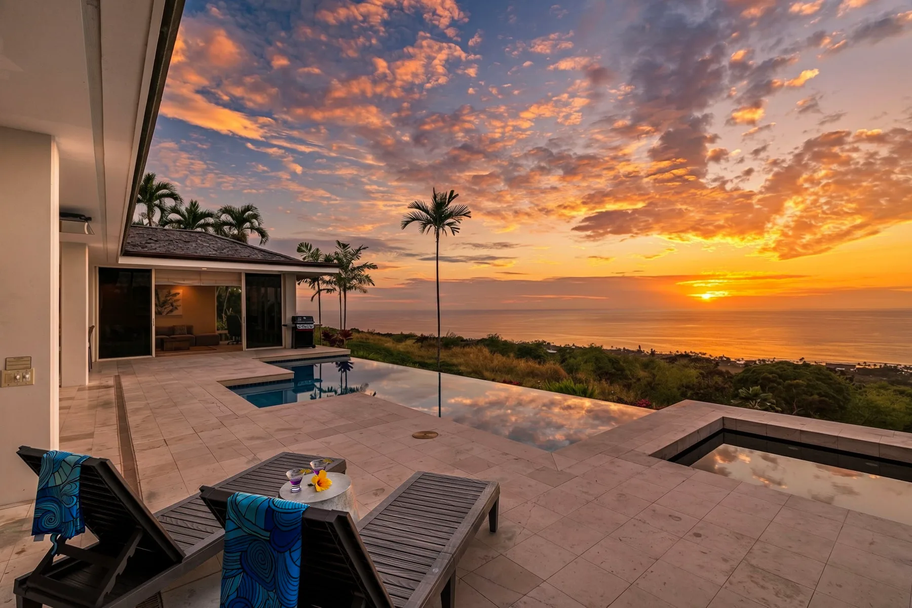 Un patio exterior de baldosas da a una piscina y al mar al atardecer.