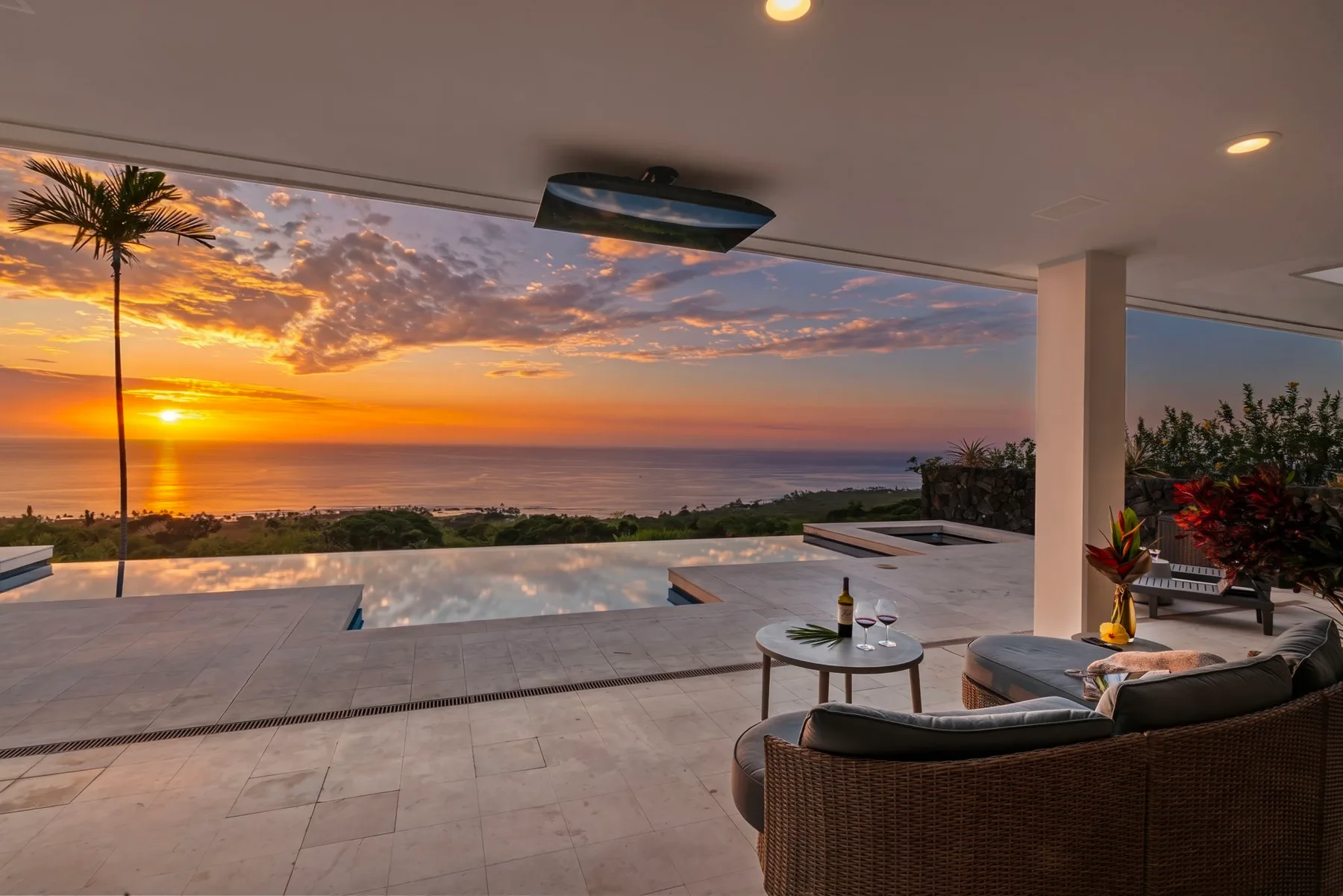 Una zona de estar al aire libre y cubierta da a una piscina y al océano al atardecer.