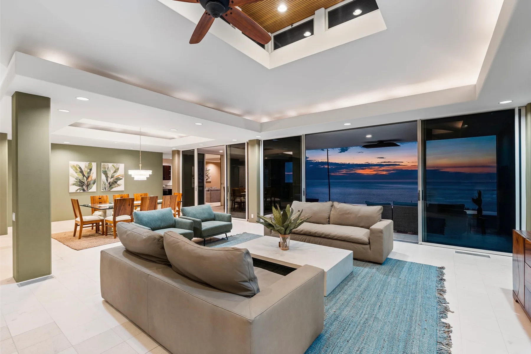 Una sala y comedor de concepto abierto con vista al océano al atardecer.