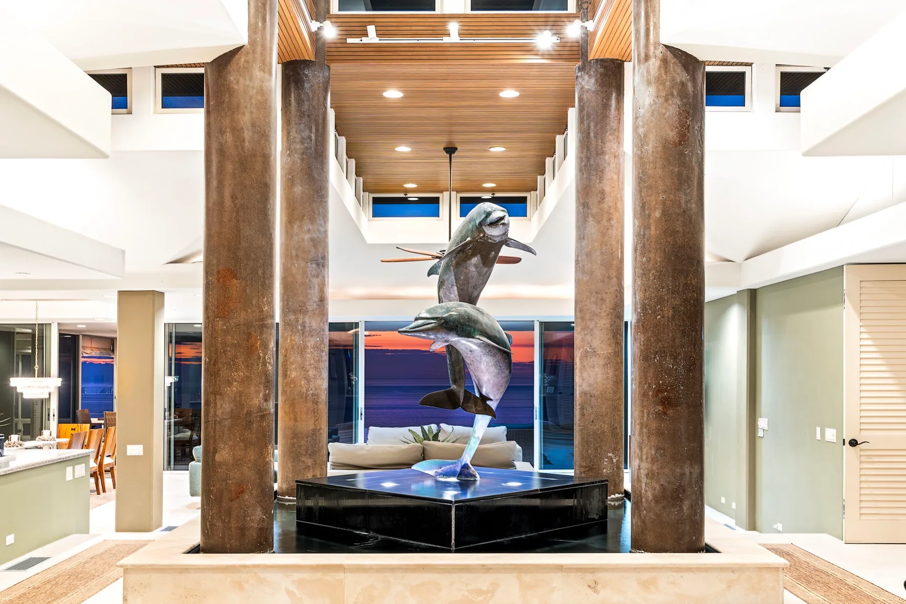 Un amplio interior presenta una escultura de delfines sobre un pedestal central entre columnas altas.