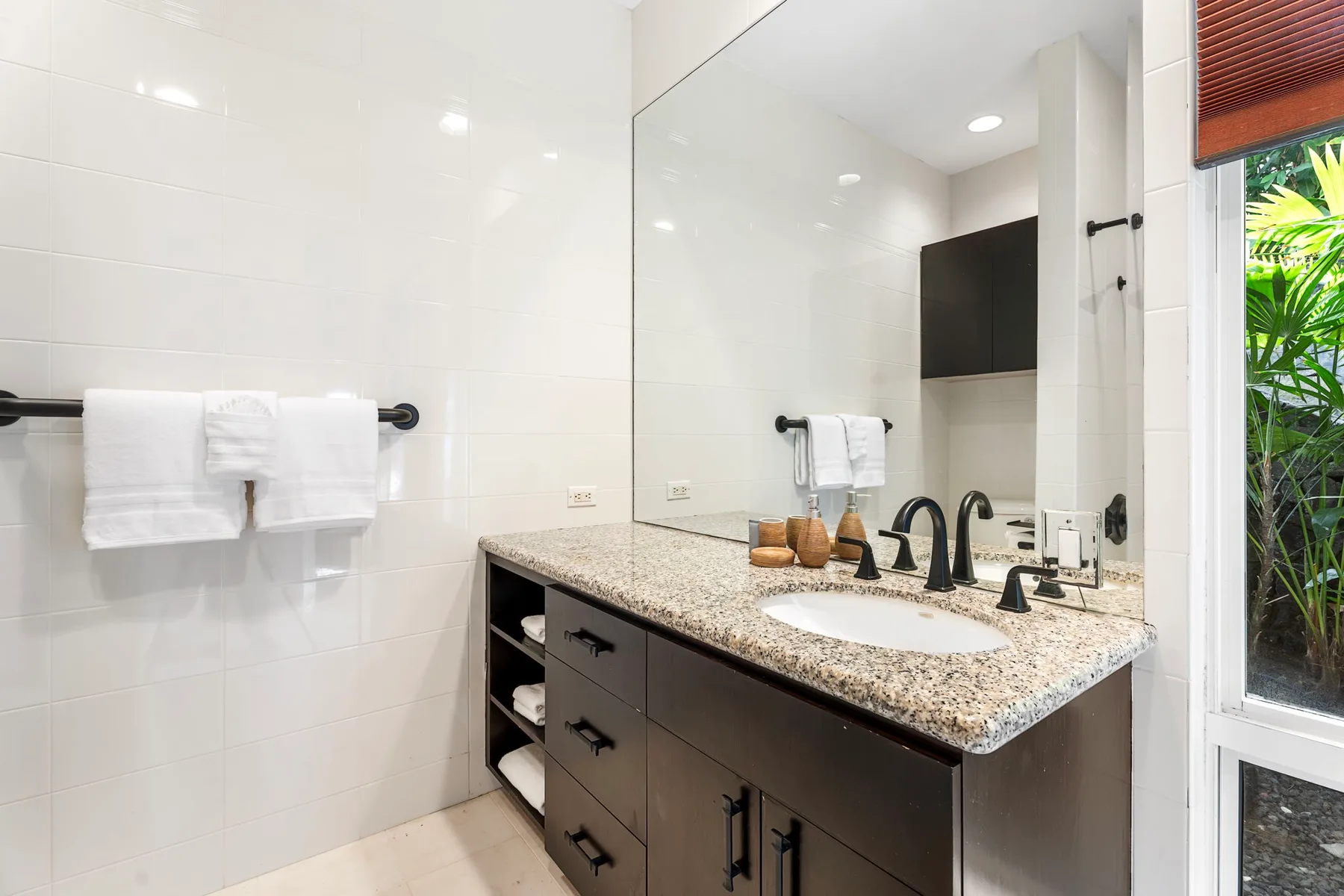 Un baño luminoso con un tocador amplio, espejo y paredes de azulejos blancos.