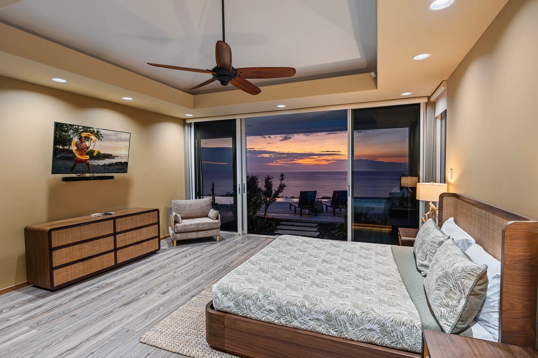 Un dormitorio con una cama grande frente a puertas corredizas de vidrio y una vista al atardecer.