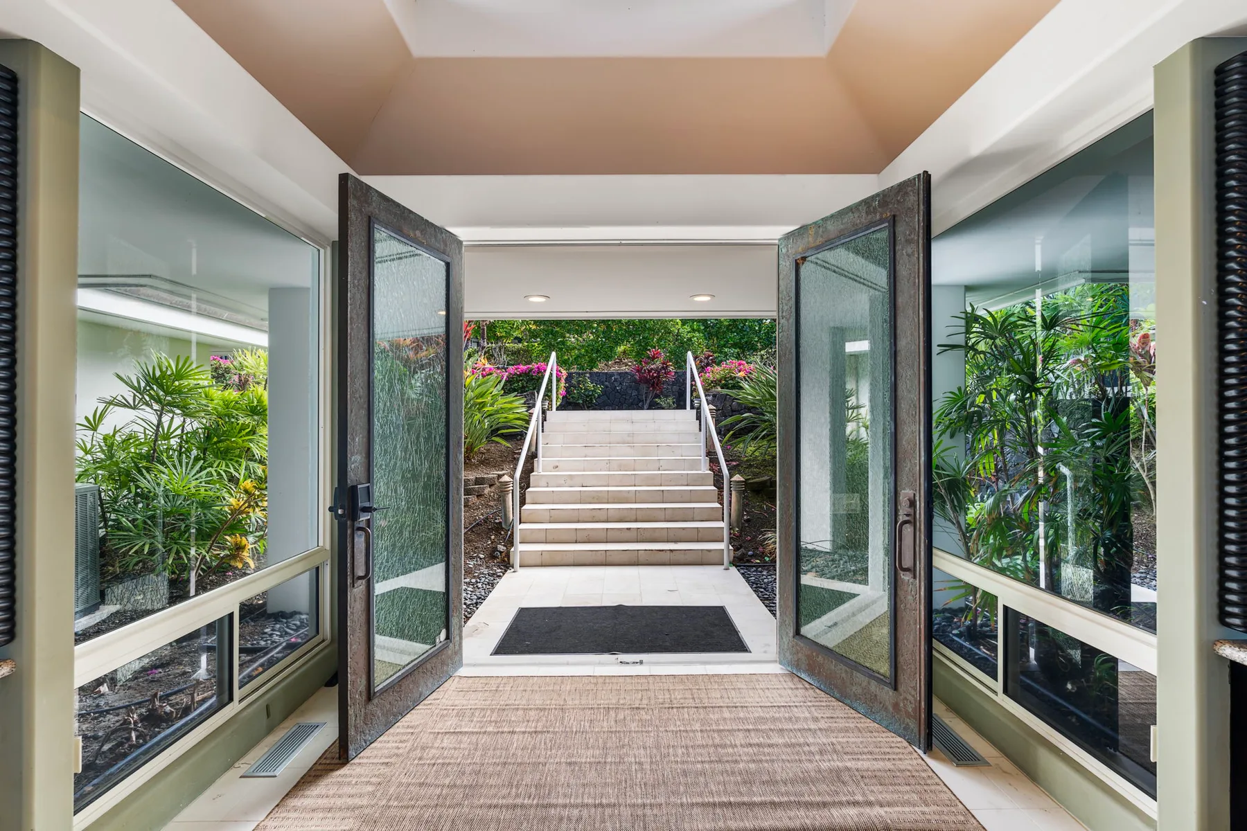 Una puerta de vidrio abierta da a escalones exteriores rodeados de vegetación.