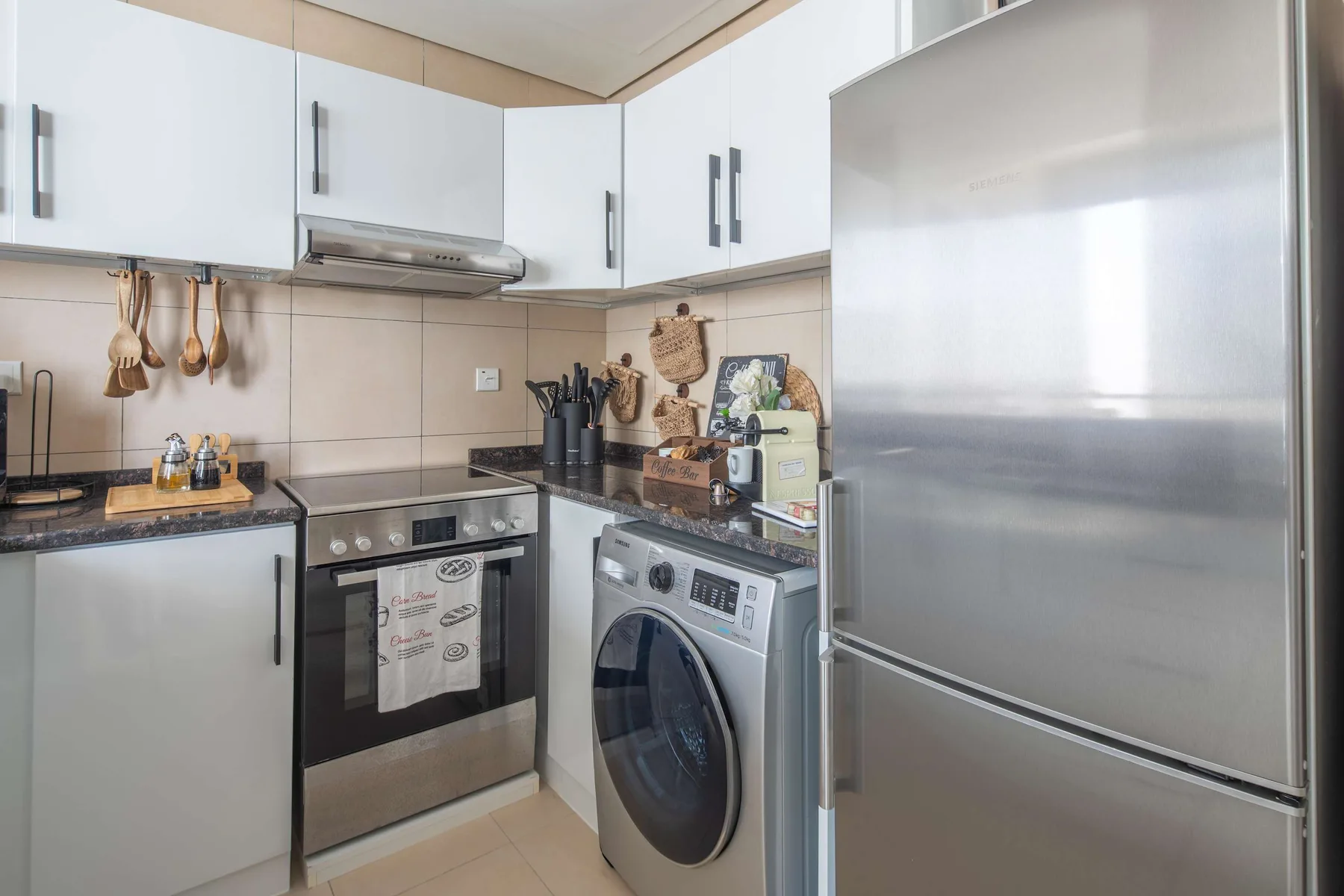 Una cocina compacta con armarios blancos, estufa, lavadora y refrigerador.
