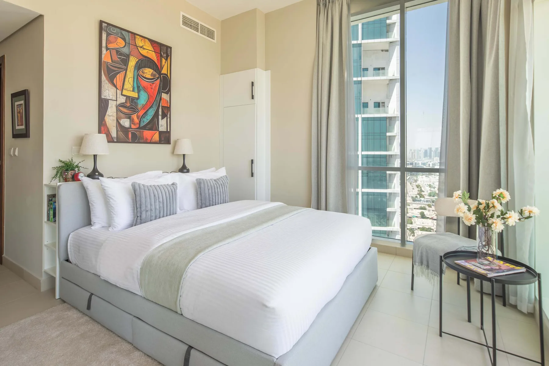 Un dormitorio luminoso con una cama tendida junto a una ventana grande.