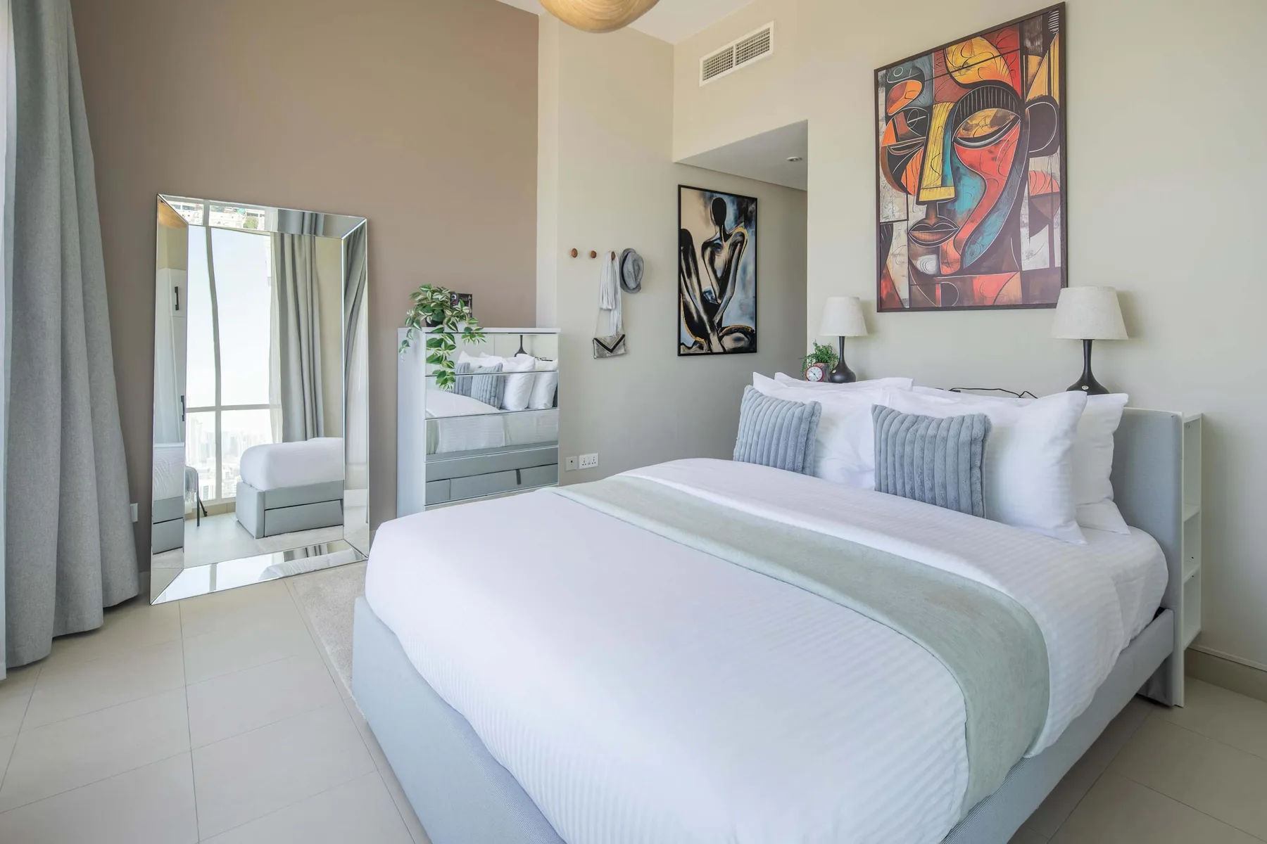 Un dormitorio luminoso con una cama tendida y una obra colorida sobre el cabecero.