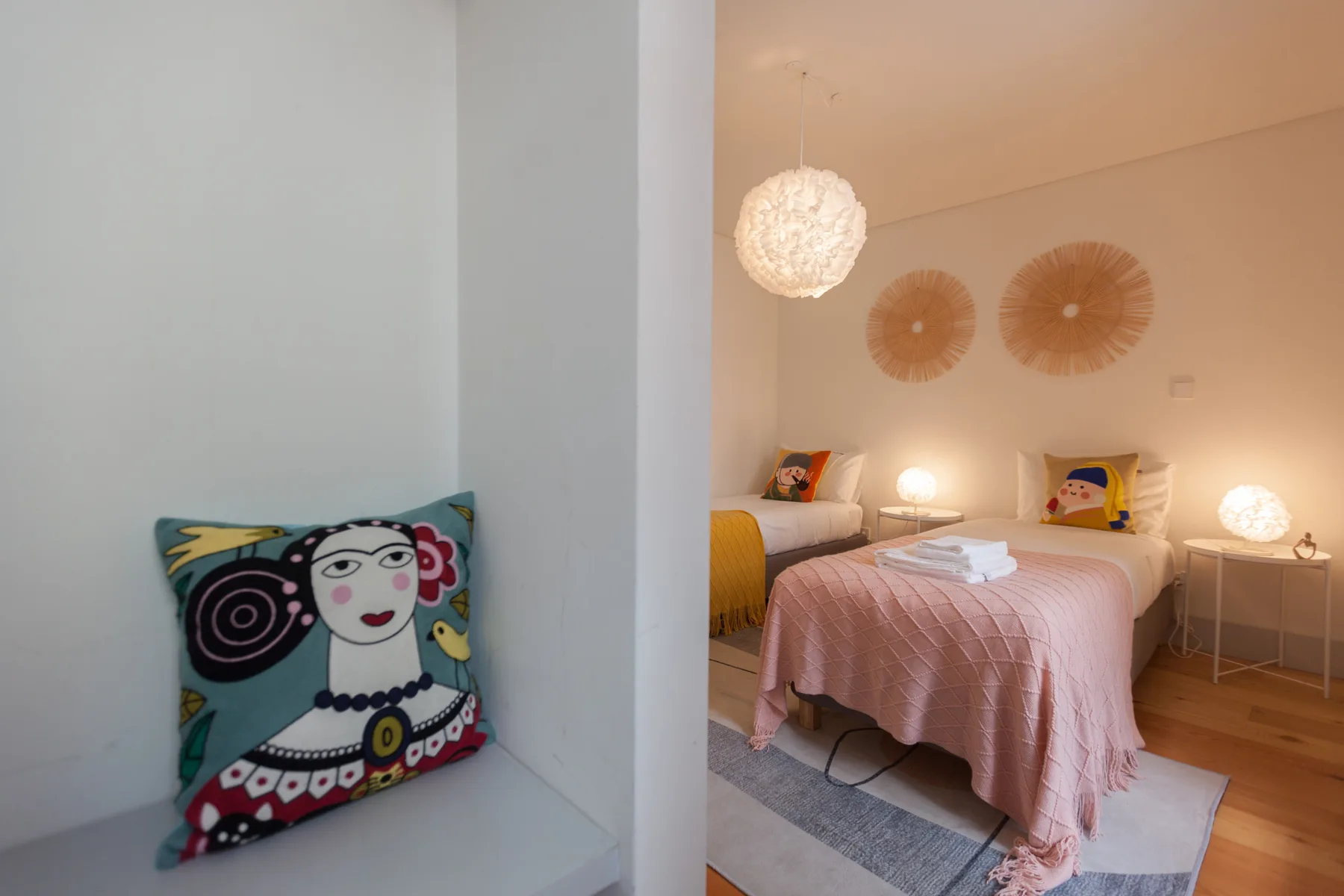 A bedroom with a pink bedspread, decorative wall fans, and bedside lamps.