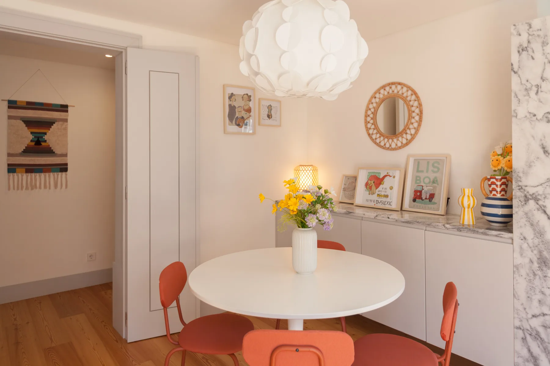 A dining area with a round table, red seating, and flowers.