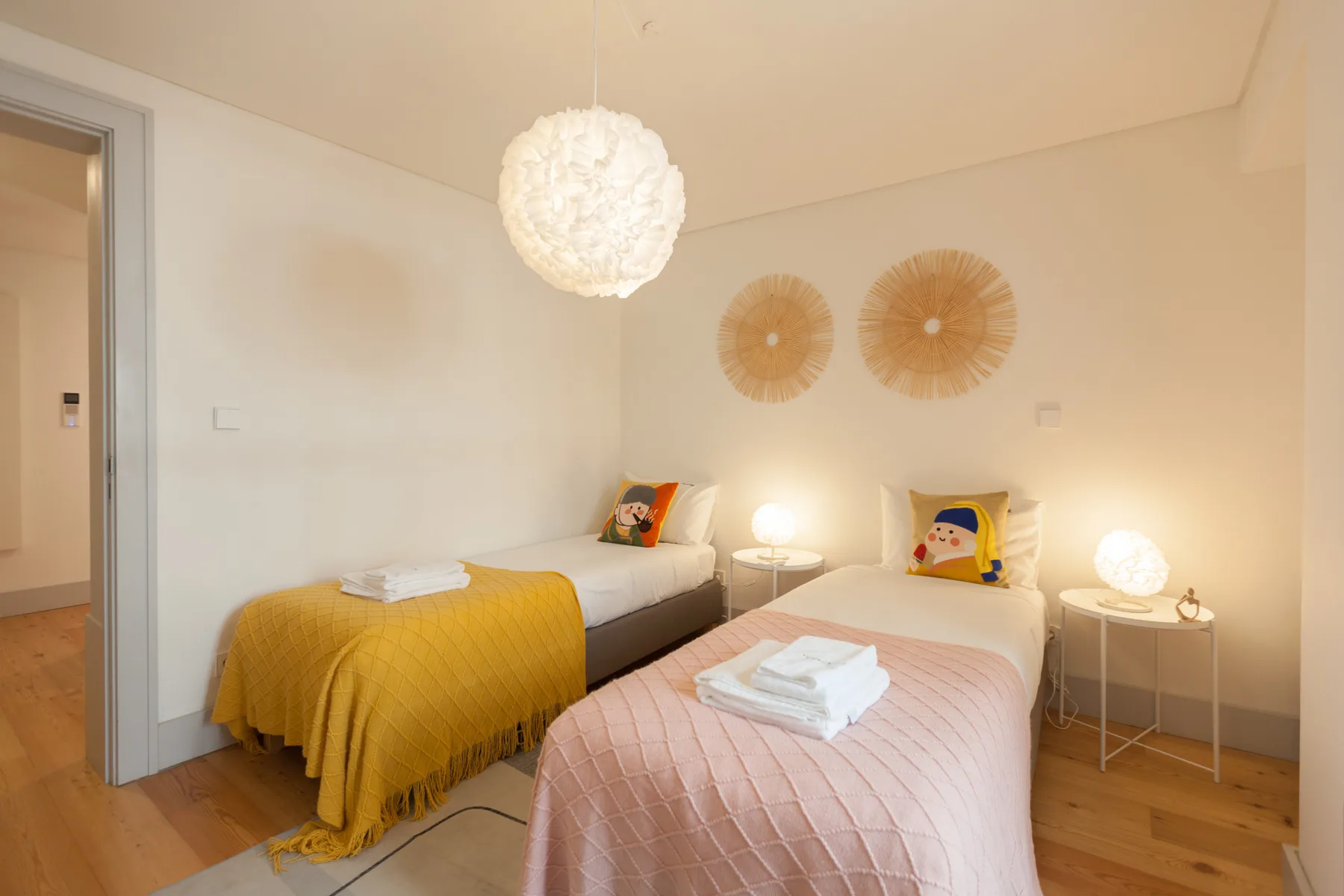 A bedroom with two beds, colorful bedding, and warm bedside lighting.