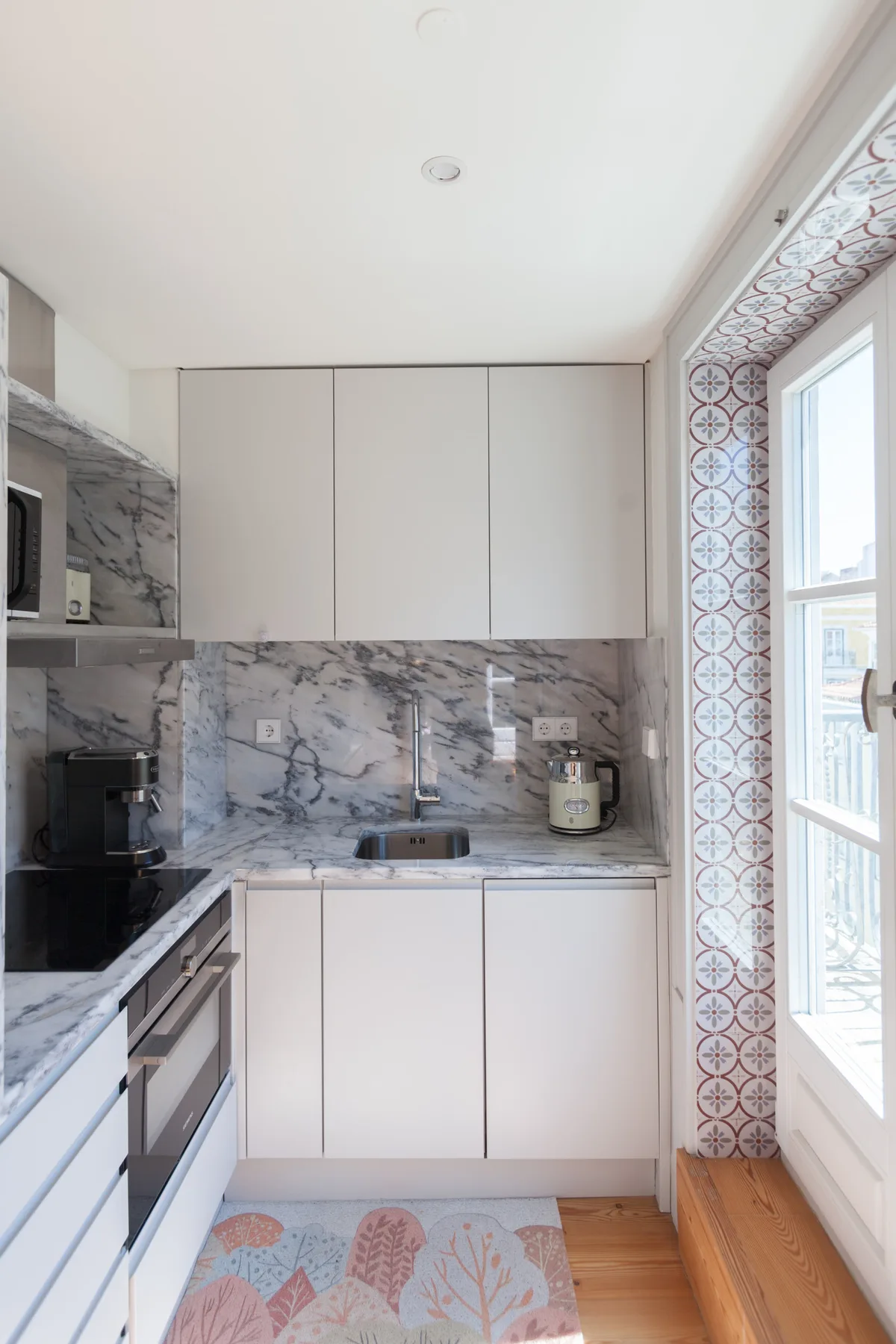 A bright kitchen with white cabinets, gray countertops, and a glass door.