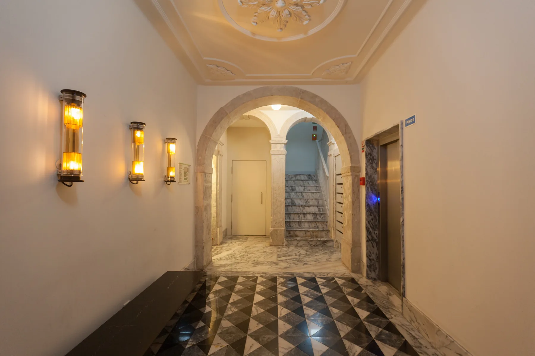 An ornate hallway with a patterned floor and an arched opening to a staircase.