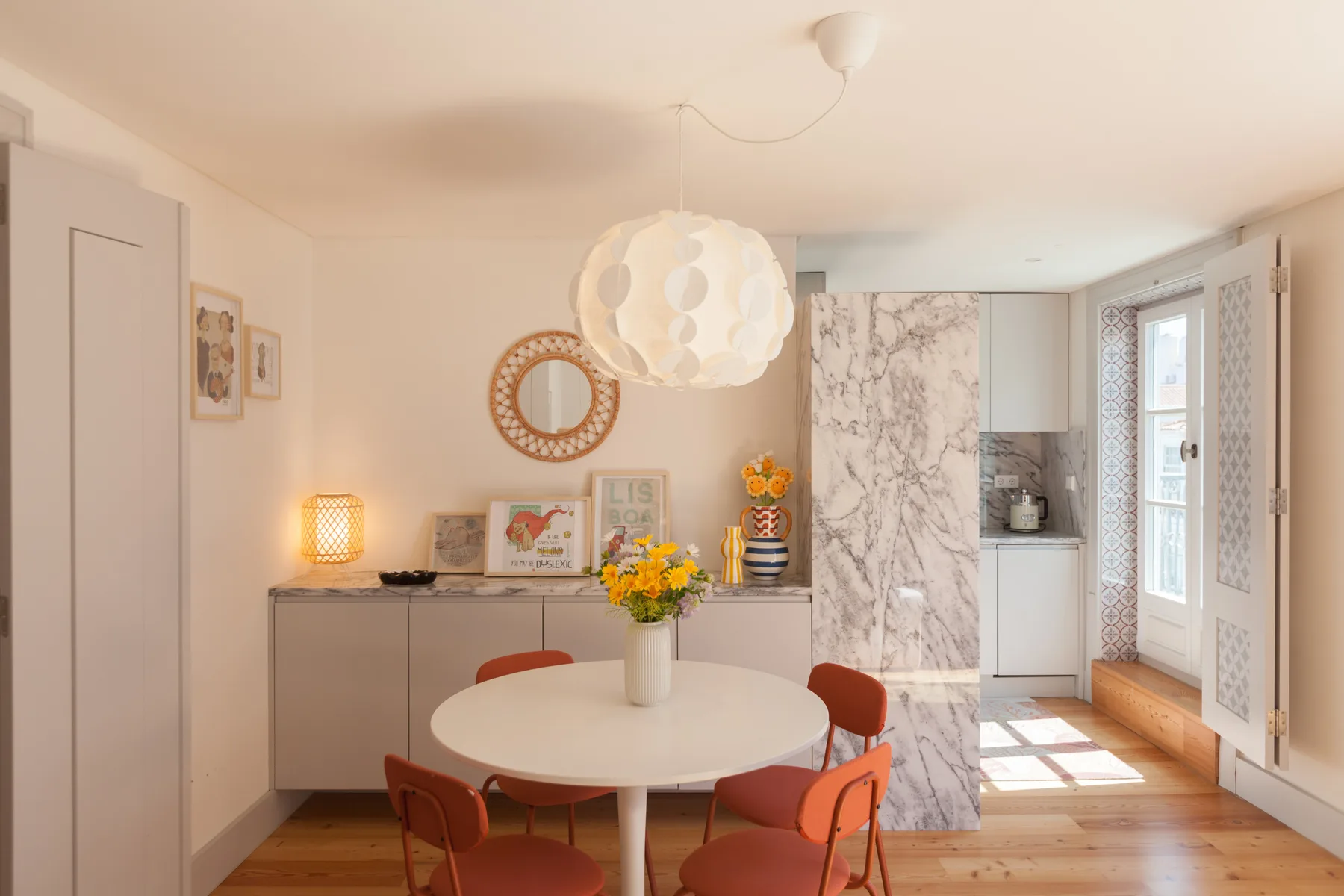 Dining area with a round table, colorful chairs, and flowers.