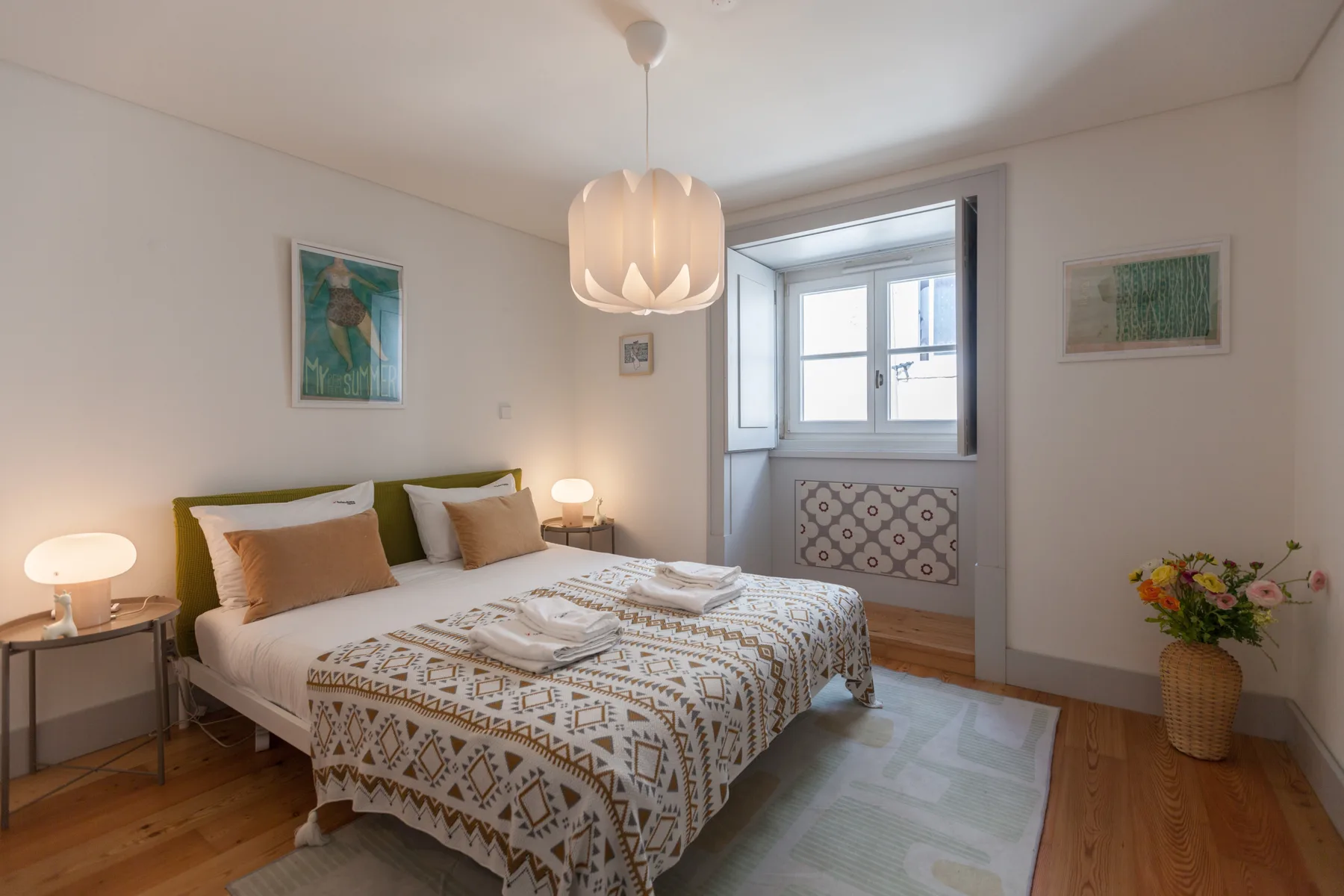 A bedroom with a double bed, bedside tables, and a window.