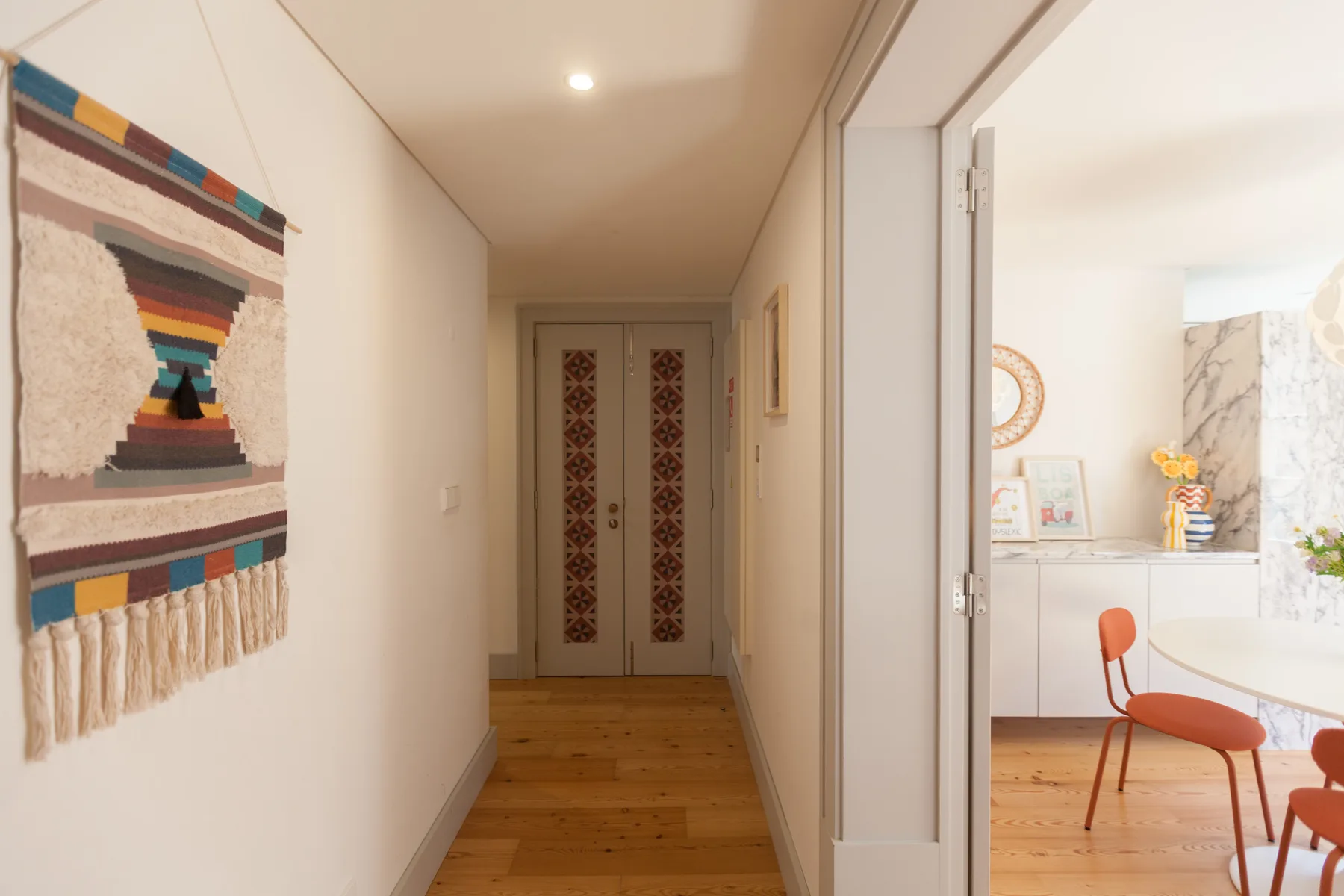 A hallway leads toward a bright dining area with a table and chairs.