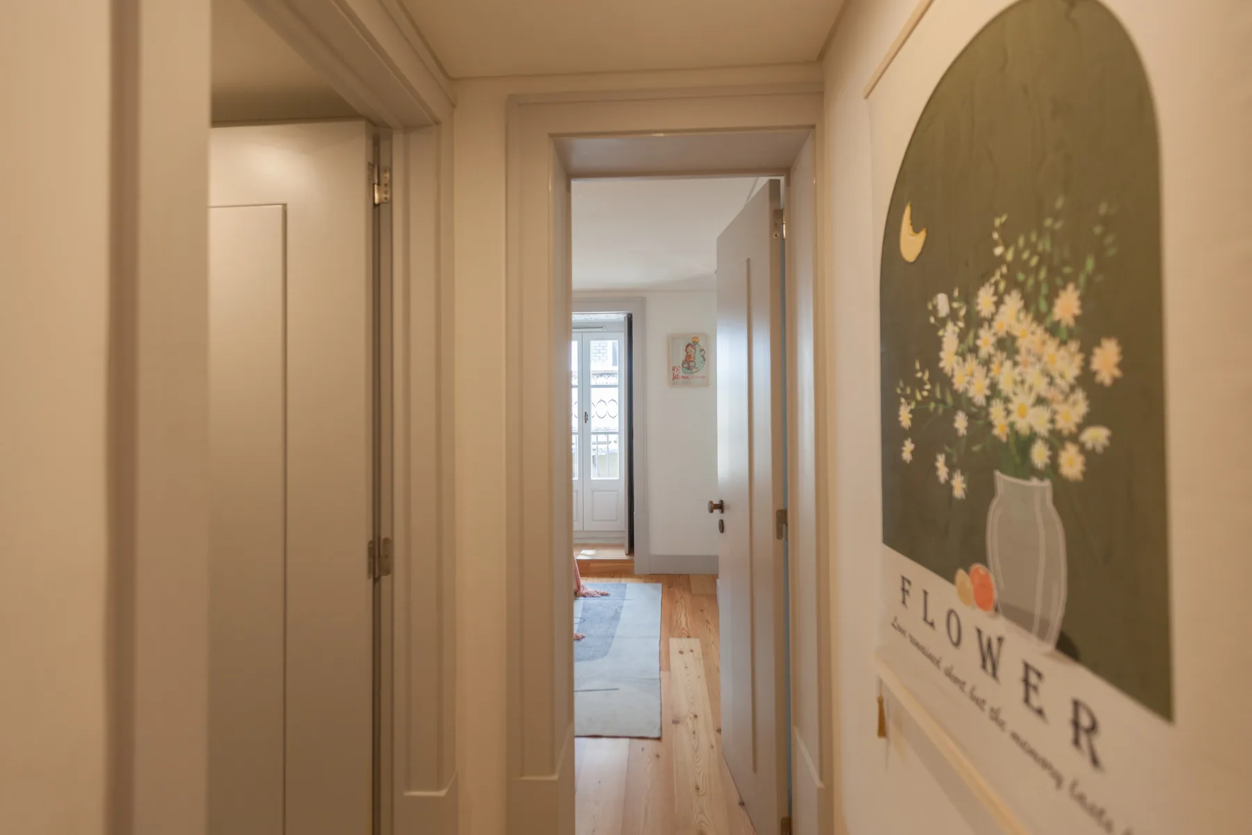 A hallway leads toward a bright room, with a floral print on the wall.
