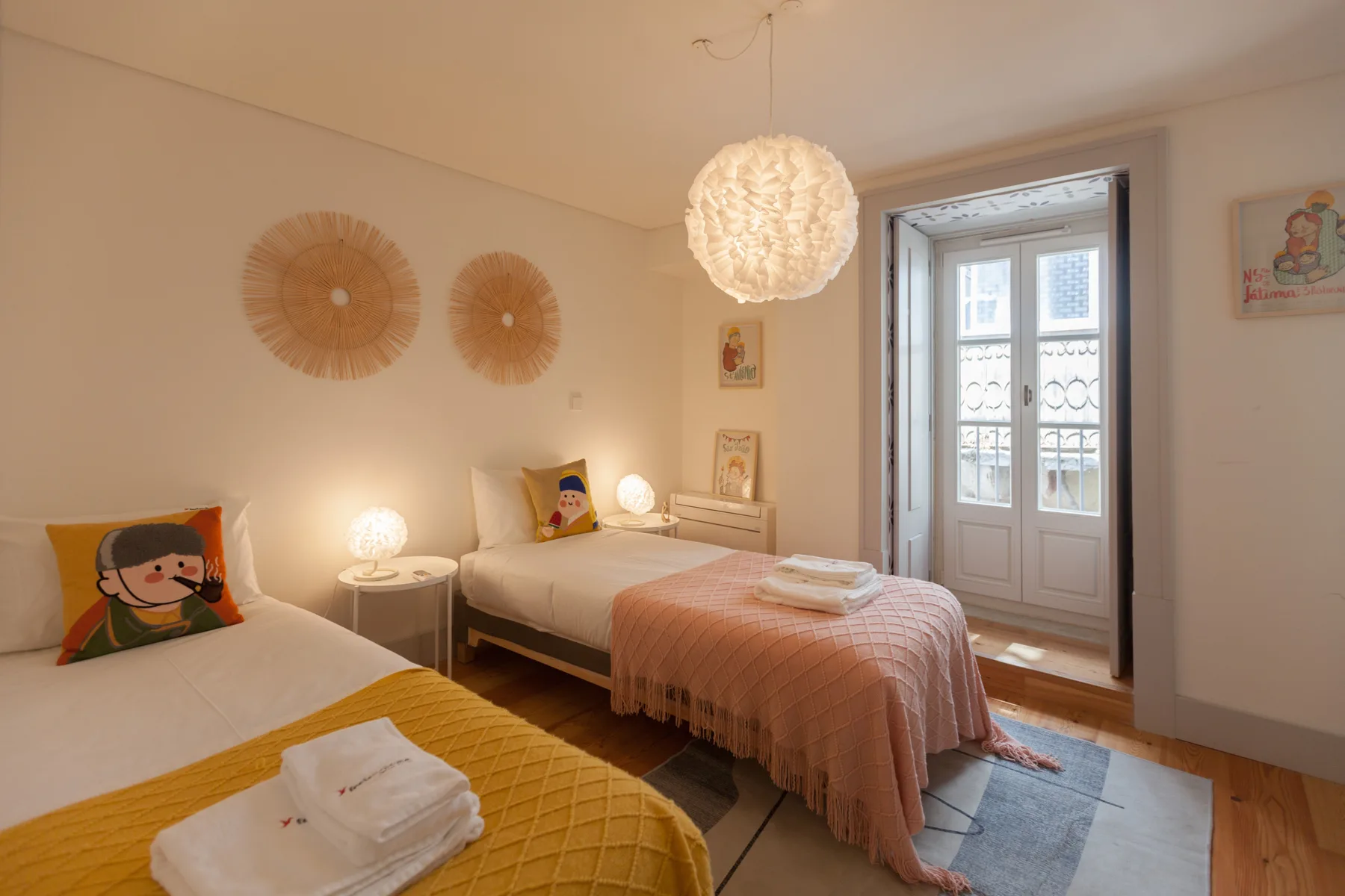 A bedroom with two beds, colorful cushions, and a glass balcony door.
