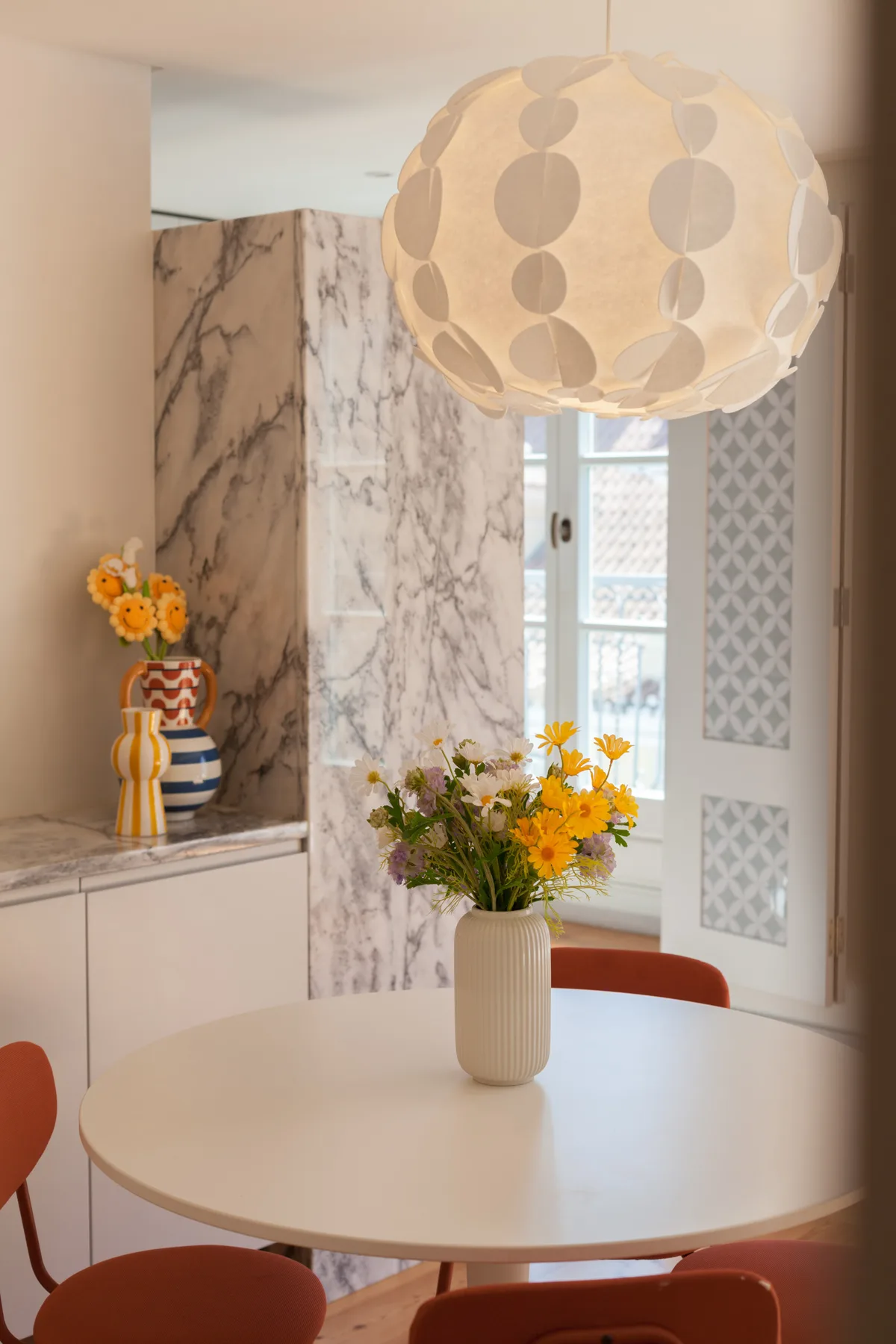 A dining area with a round table, flowers, and a large pendant lamp.