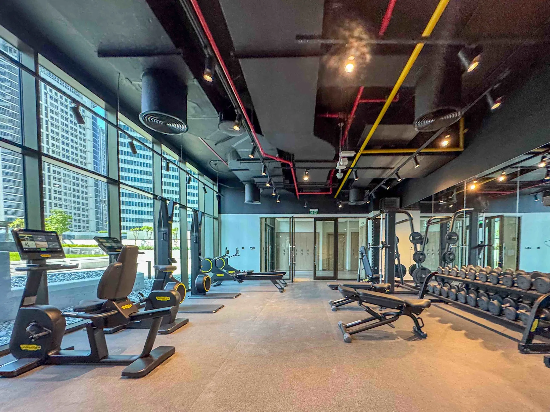Una sala de ejercicio con máquinas, pesas y grandes ventanas.