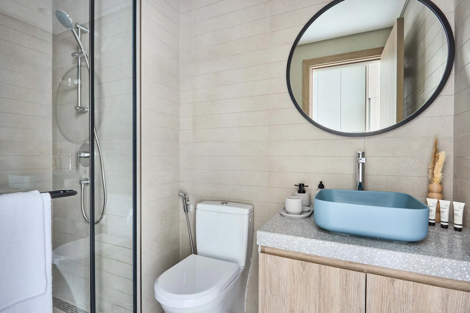 Un baño luminoso con ducha de vidrio, inodoro y lavabo azul sobre la encimera.