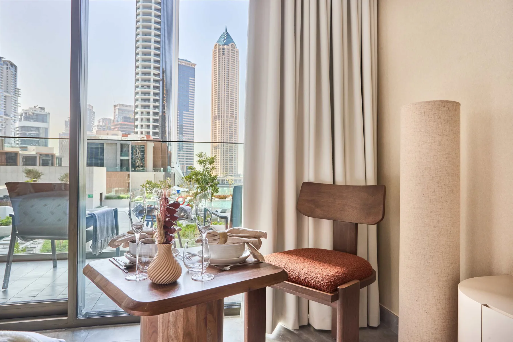 Una mesa de comedor y una silla están junto a una puerta de vidrio con vistas a edificios de la ciudad.