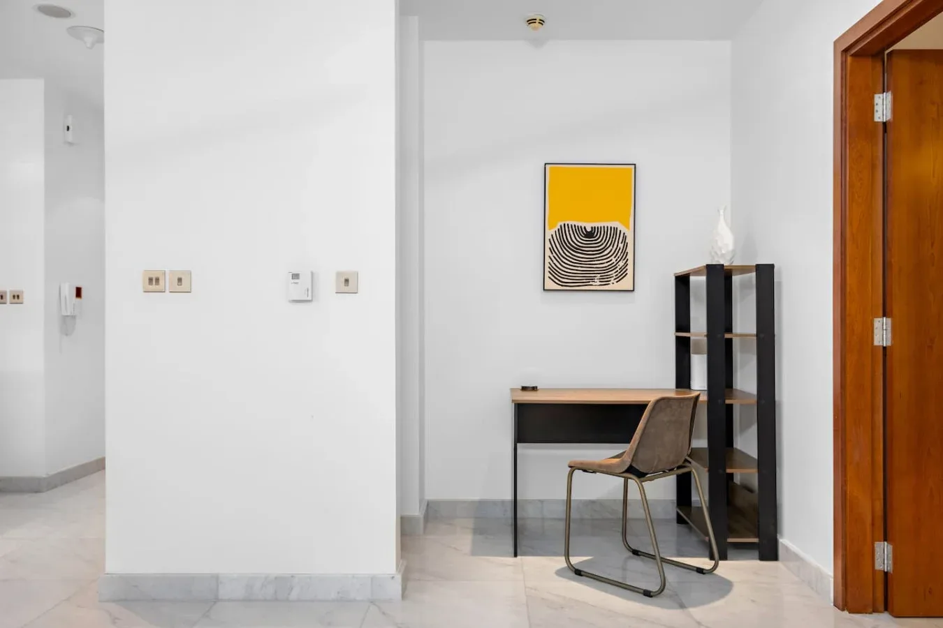 Un pequeño espacio de trabajo con escritorio, silla, estantería y arte enmarcado.