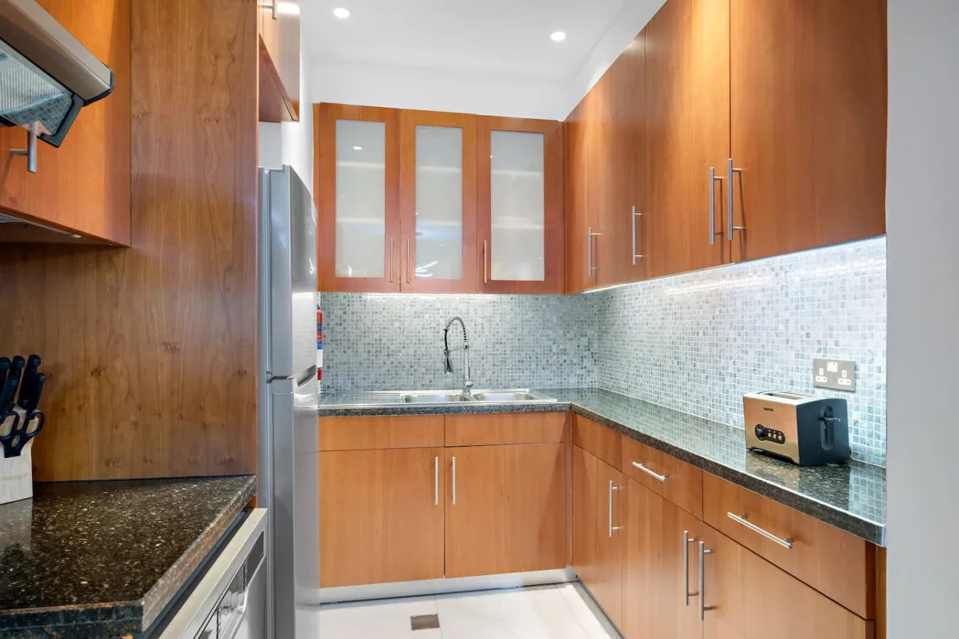 Una cocina con gabinetes de madera, encimeras oscuras y un salpicadero de azulejos.