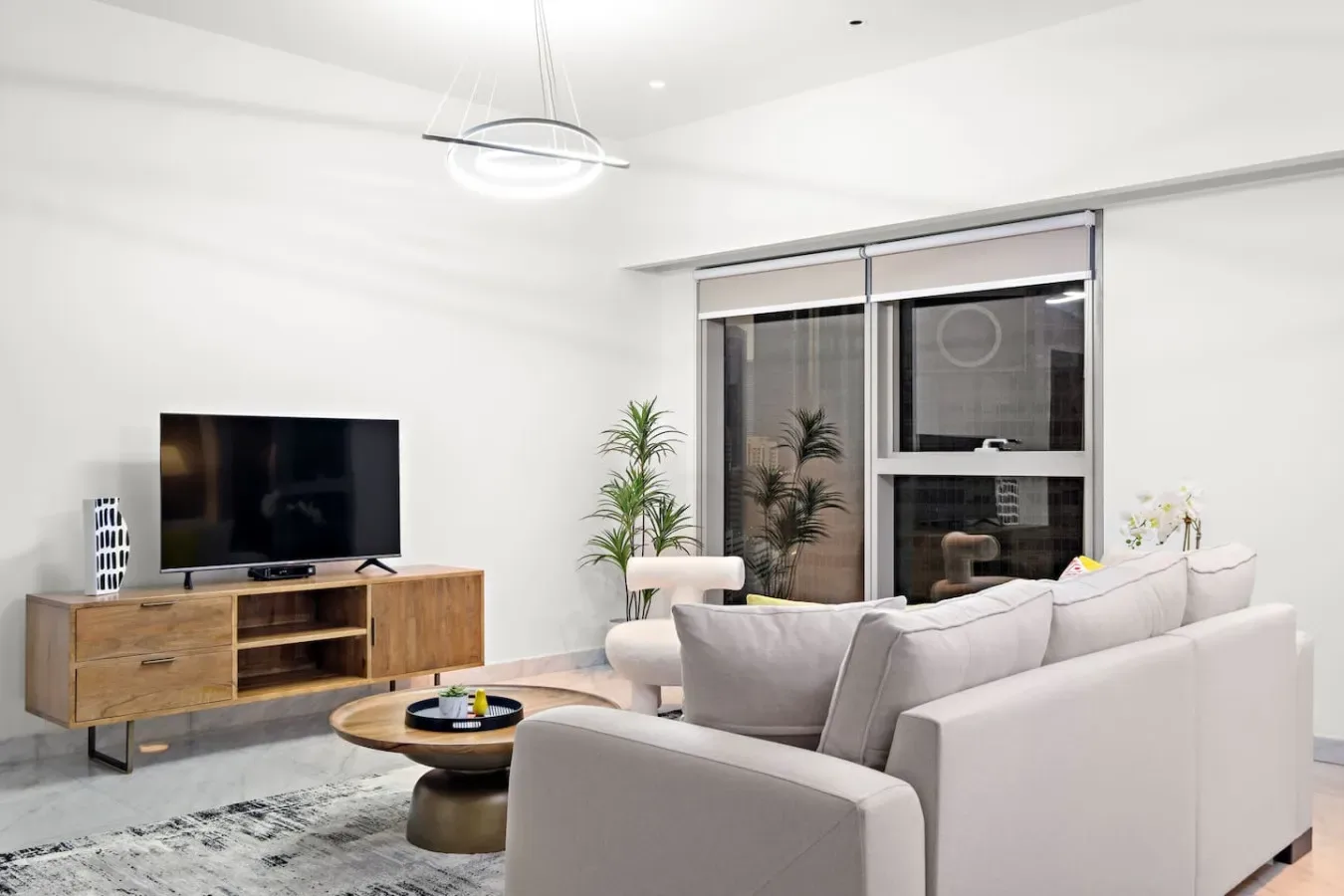 Una sala luminosa con asientos, un televisor y ventanas grandes.