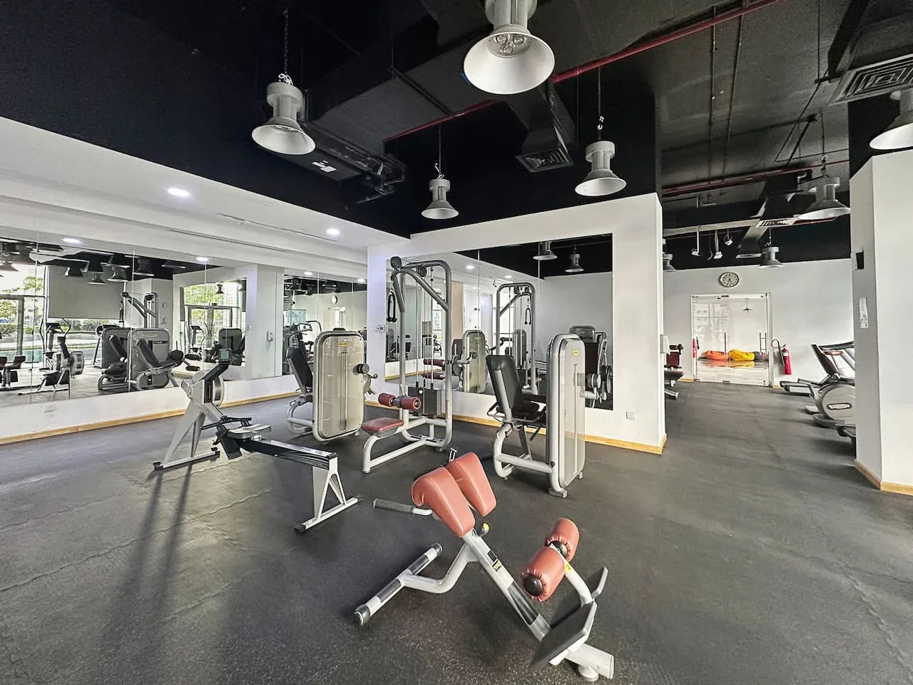 Un gimnasio con máquinas de ejercicio y bancos de pesas bajo luces de techo.