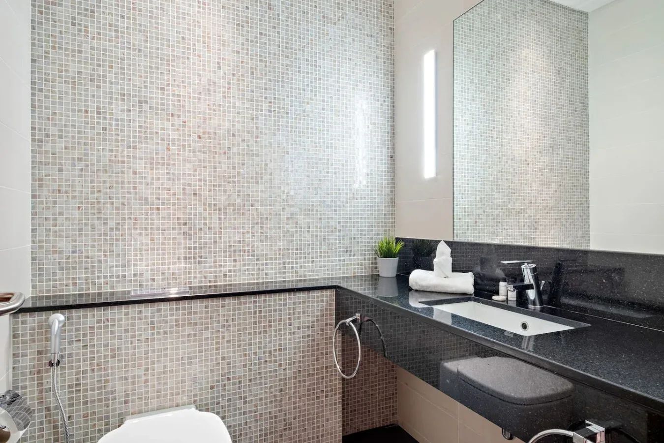 Un baño con azulejos, inodoro, lavabo y encimera oscura.