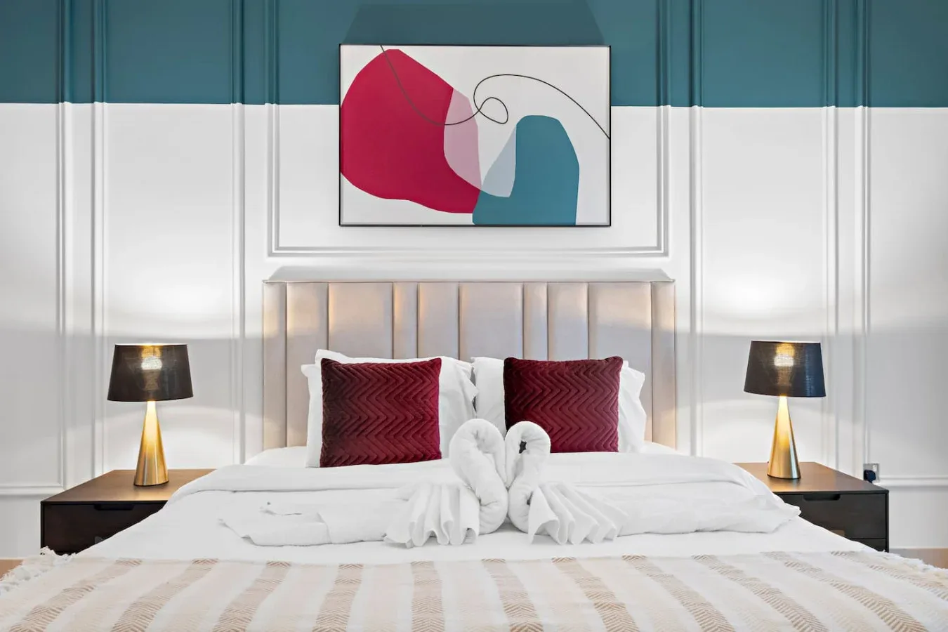 Un dormitorio con una cama bien arreglada, lámparas a juego y arte abstracto enmarcado.