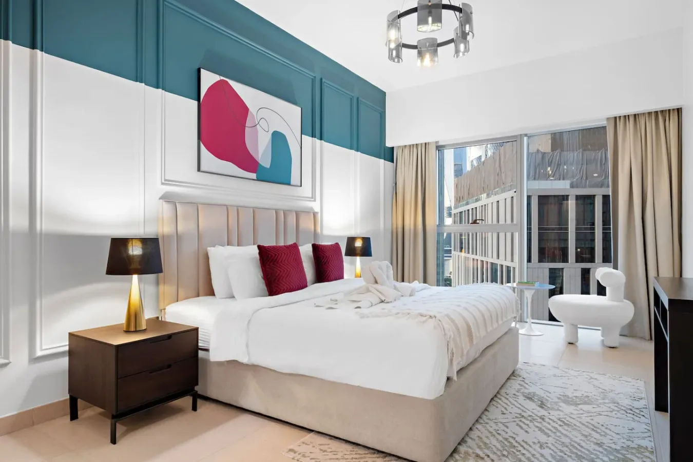 Un dormitorio con una cama grande, arte abstracto y ventanas con vista a edificios cercanos.